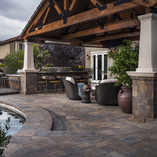 Covered pavilion with a bar counter and stools beside a pool on a paver patio