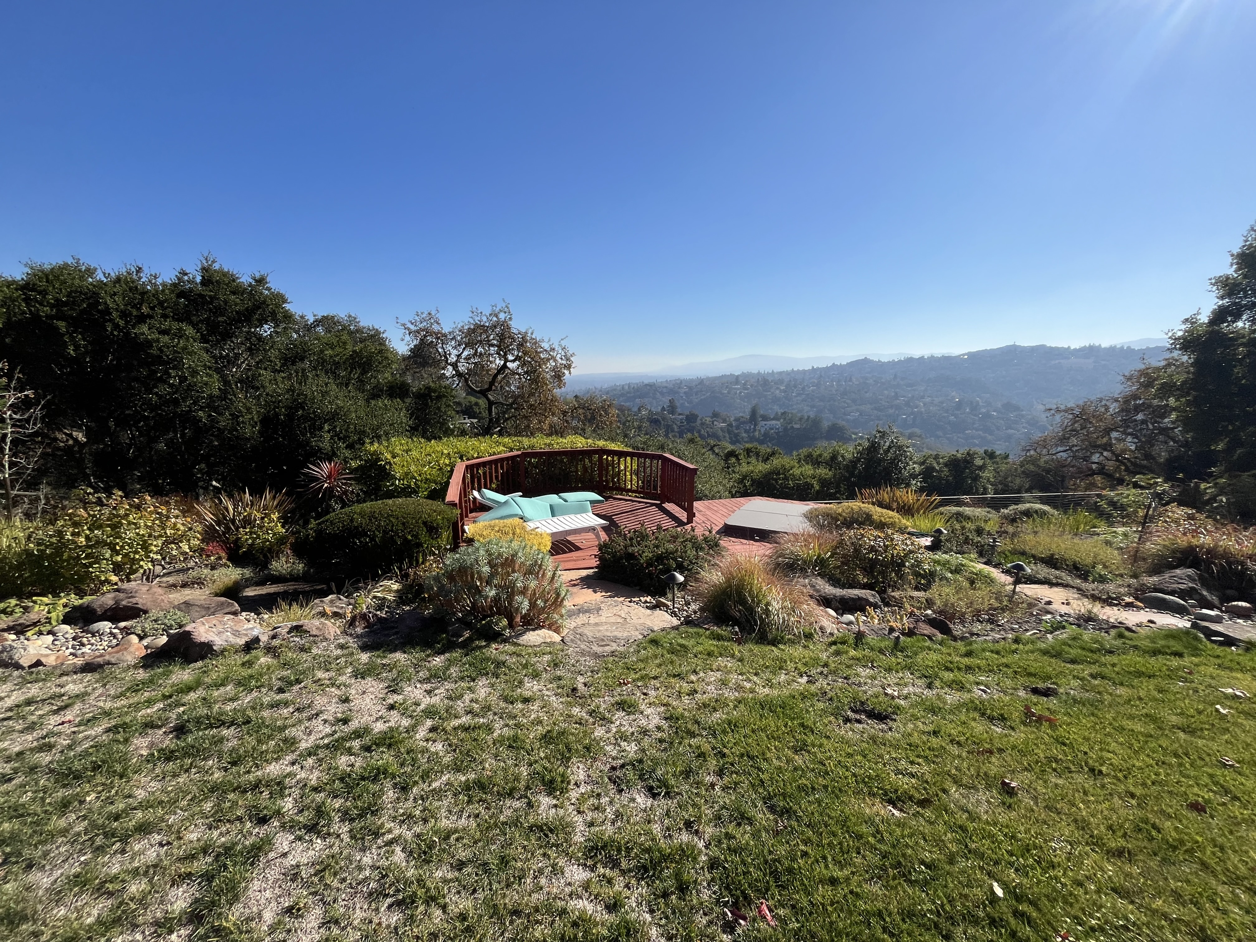 Backyard view showing a finished paver patio seating area with built-in bench and cushions overlooking a valley....