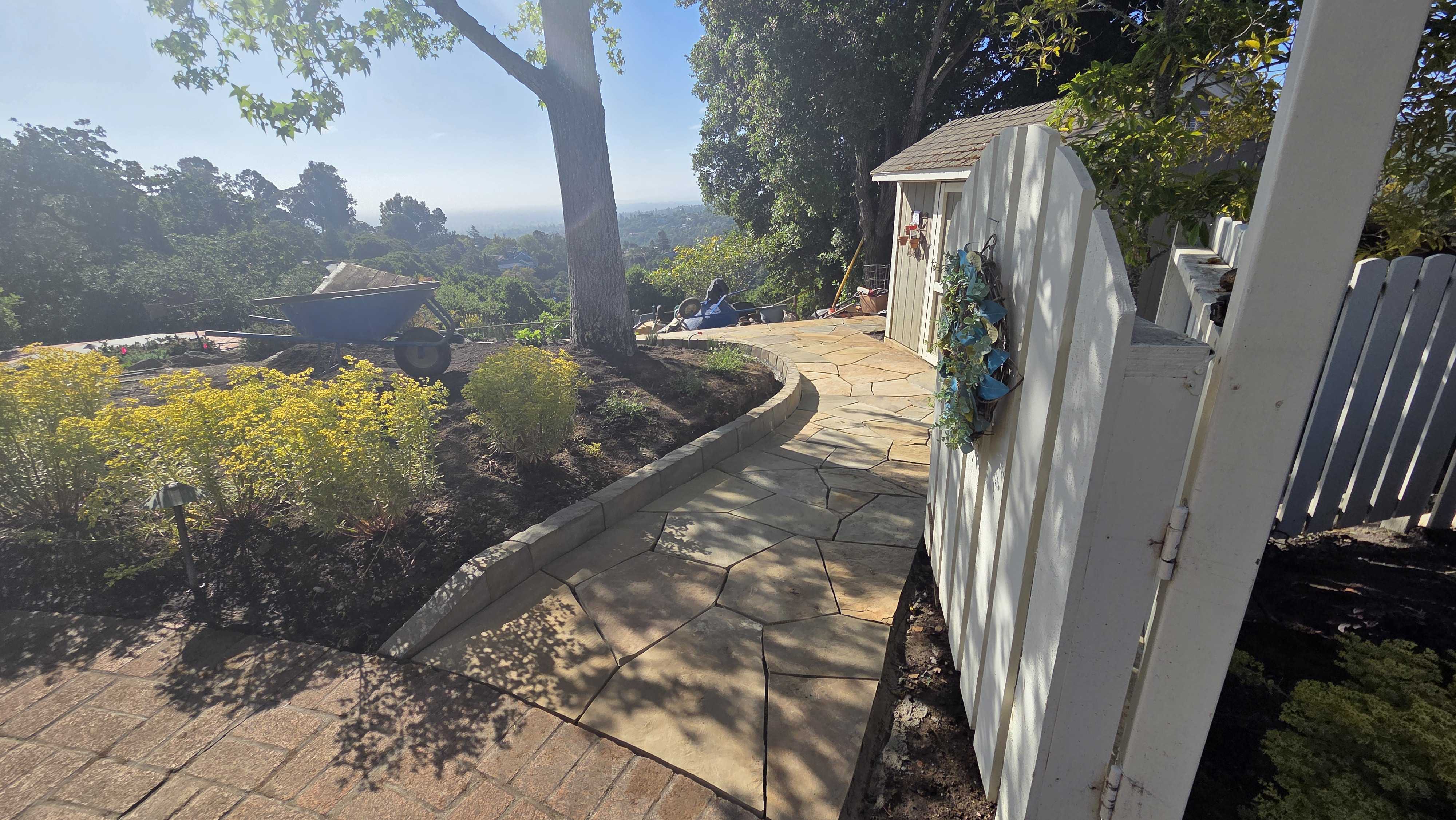 Backyard view showing a completed curved flagstone walkway flowing from an interlocking paver patio, edged by a low...