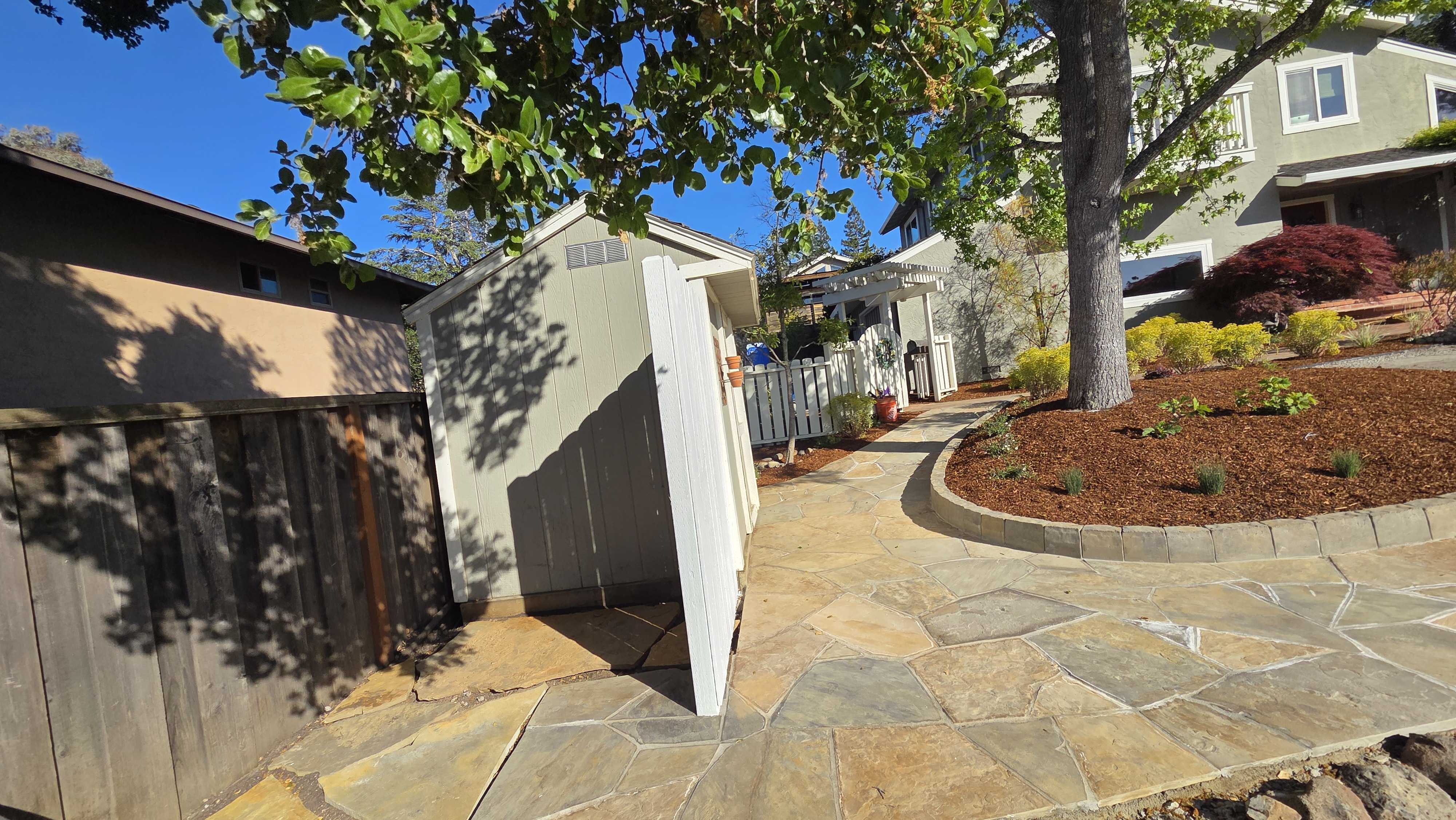 Finished irregular flagstone paver patio and walkway extend through a residential side yard with a curved stone planting...