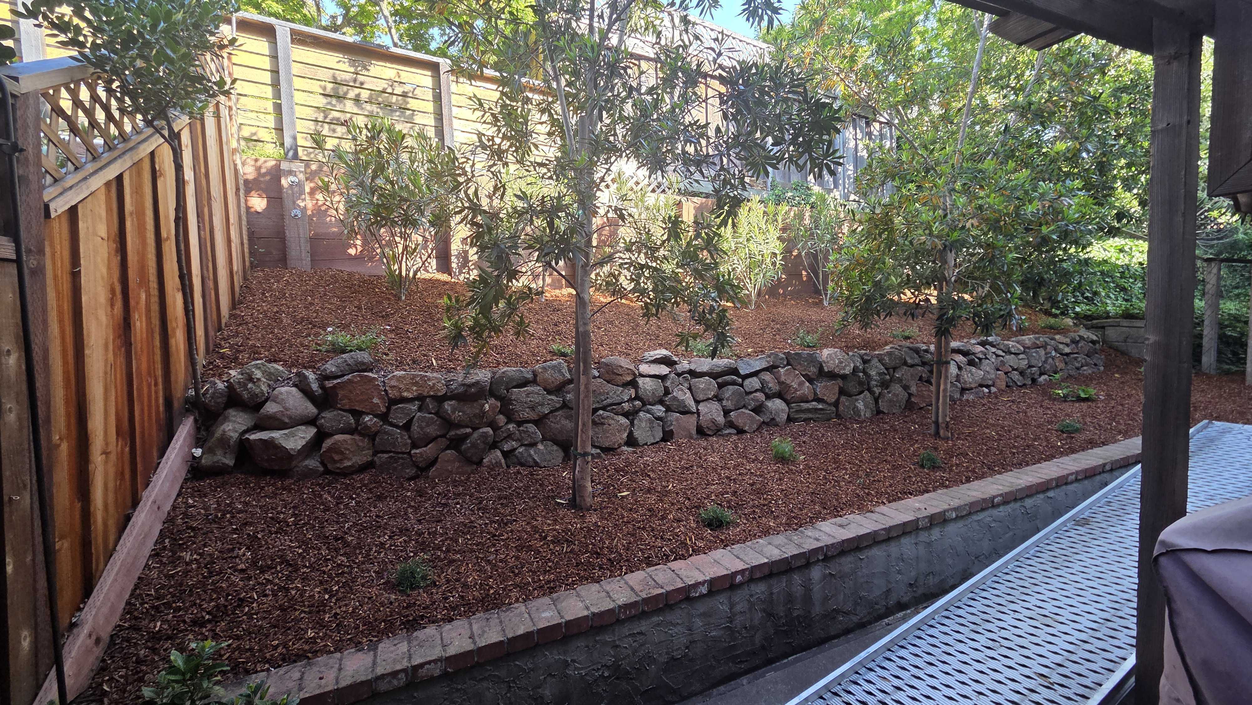 Finished backyard slope featuring a dry-stacked stone retaining wall with mulch planting beds and newly installed small...
