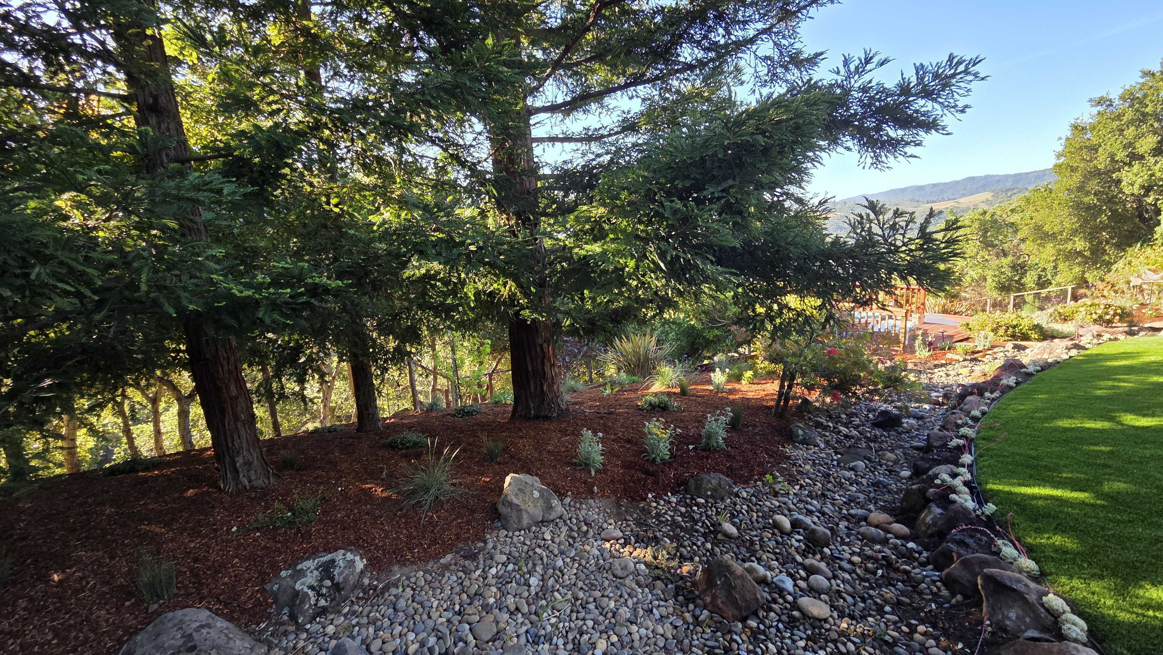 Finished backyard landscape showing artificial turf on the right with a rock-lined dry creek/drainage swale and river...