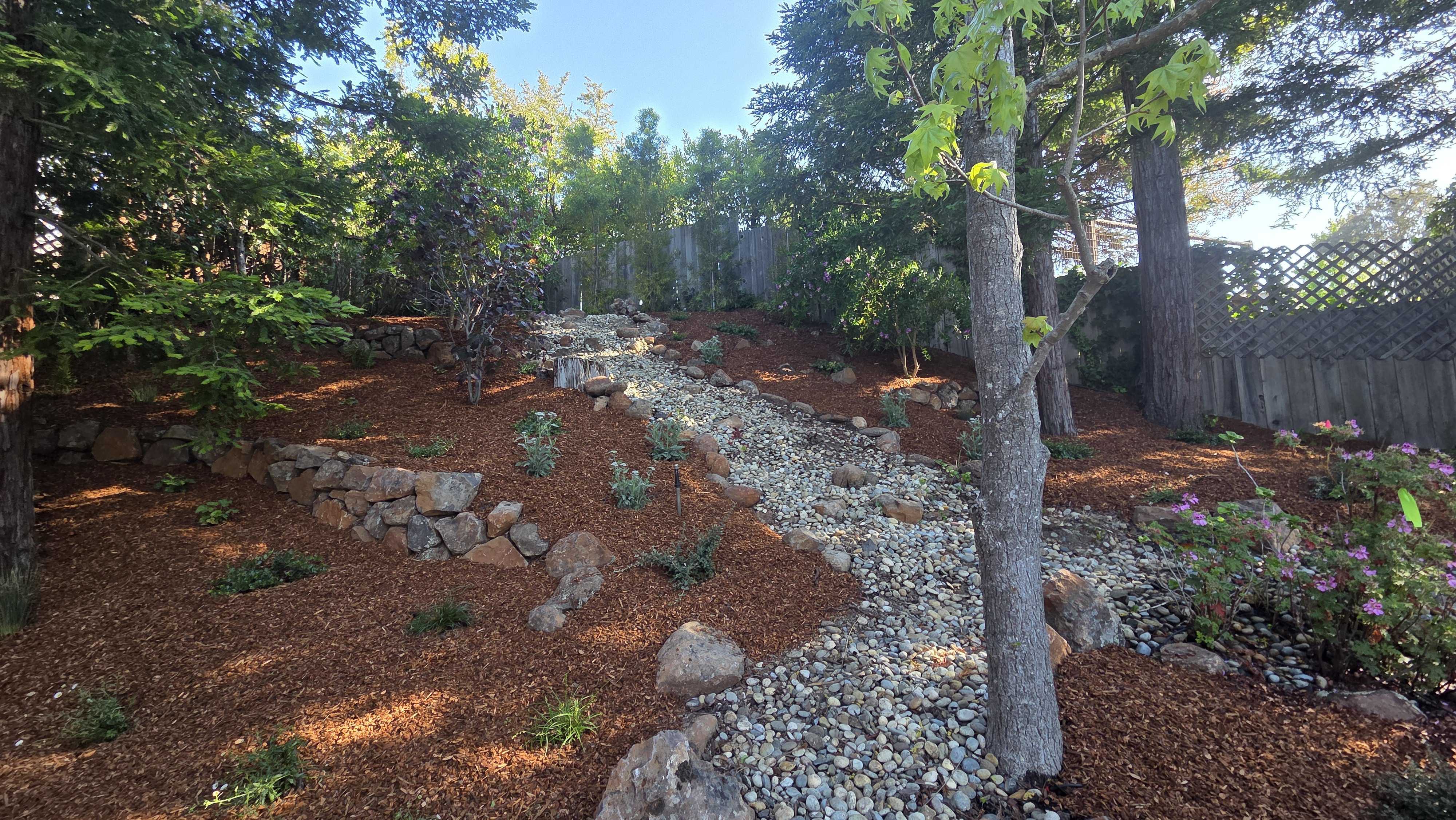Backyard slope finished with a dry creek bed of river rock and strategically placed boulders, surrounded by fresh mulch...