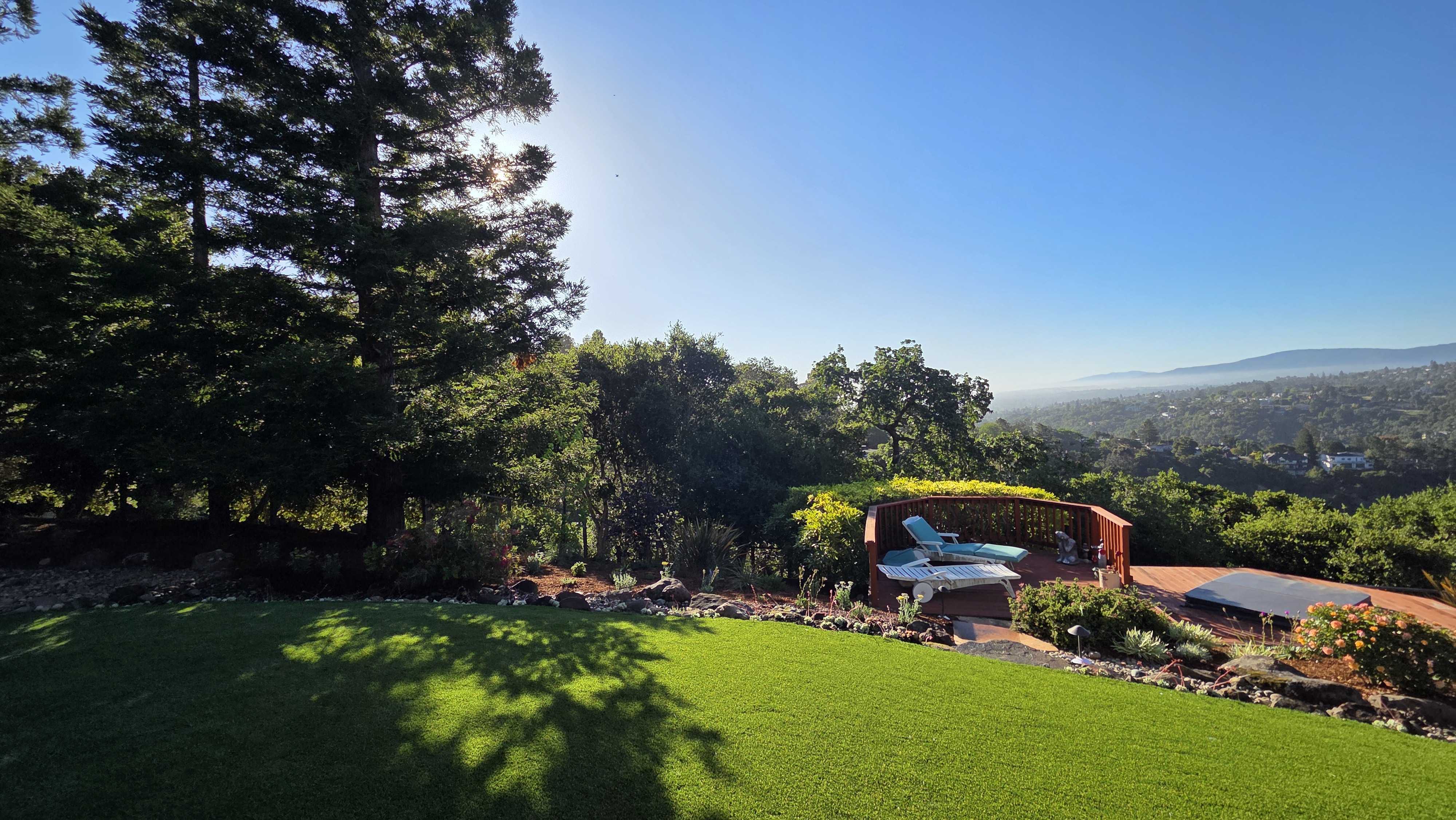 Finished residential backyard showing a clean installation of artificial turf adjacent to a patio/deck and low retaining...