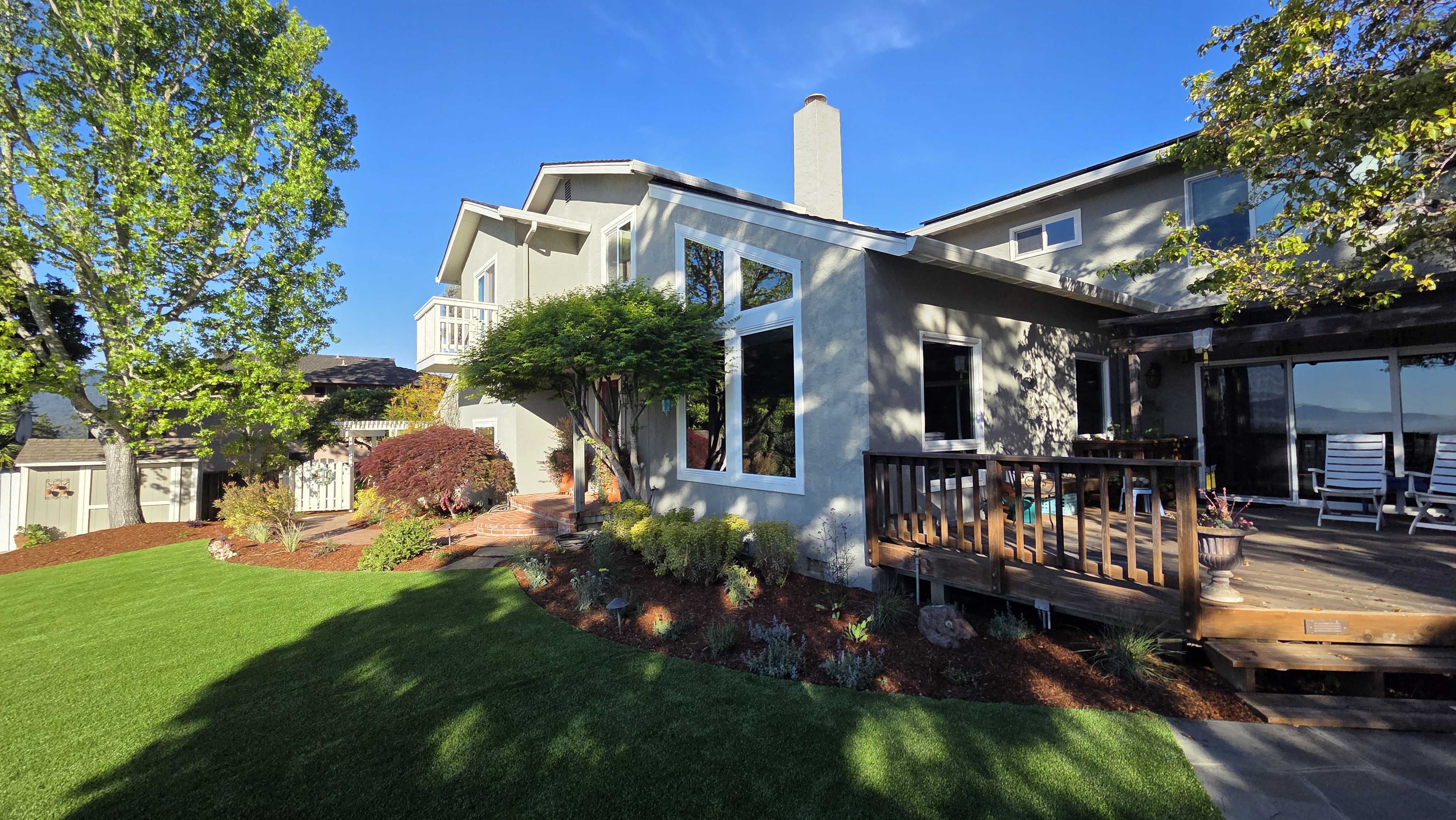 Residential backyard showing a completed landscape with newly installed artificial turf adjacent to planting beds and...
