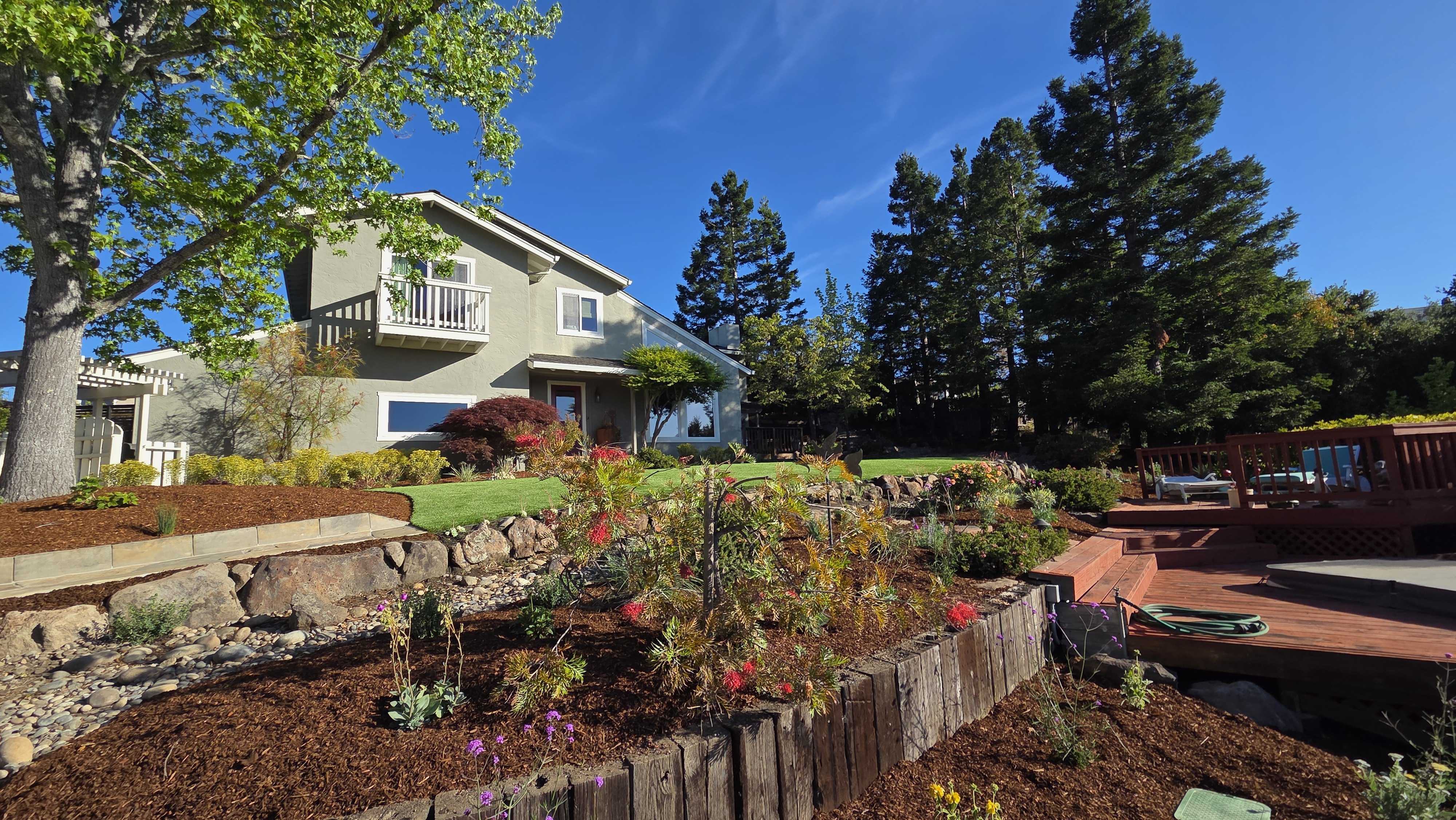 Residential backyard showing a multi-tiered landscape with timber sleeper and stone retaining walls forming raised...