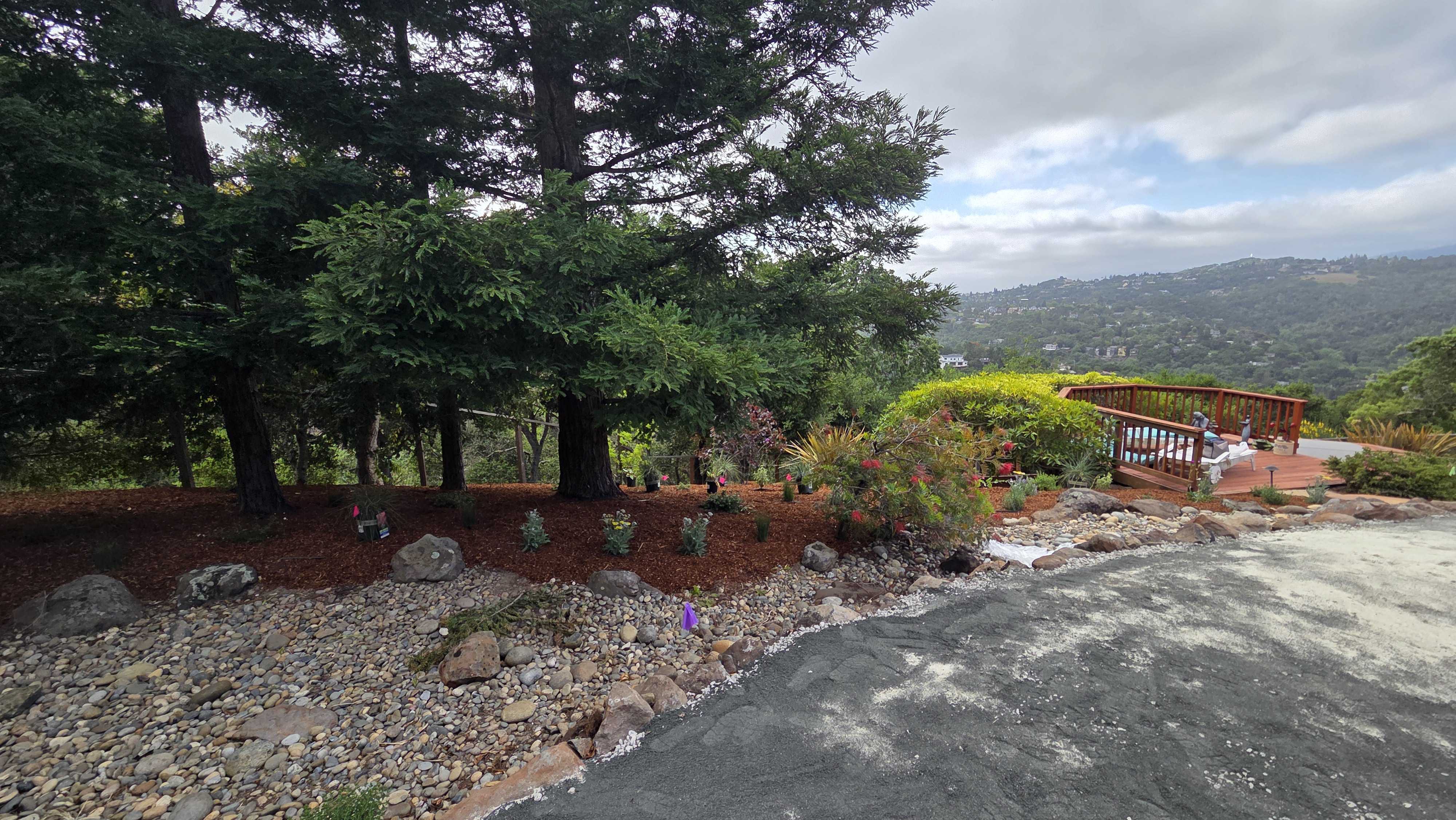 Backyard site photo showing an existing concrete slab/apron adjacent to a decorative dry creek bed of river rock and...