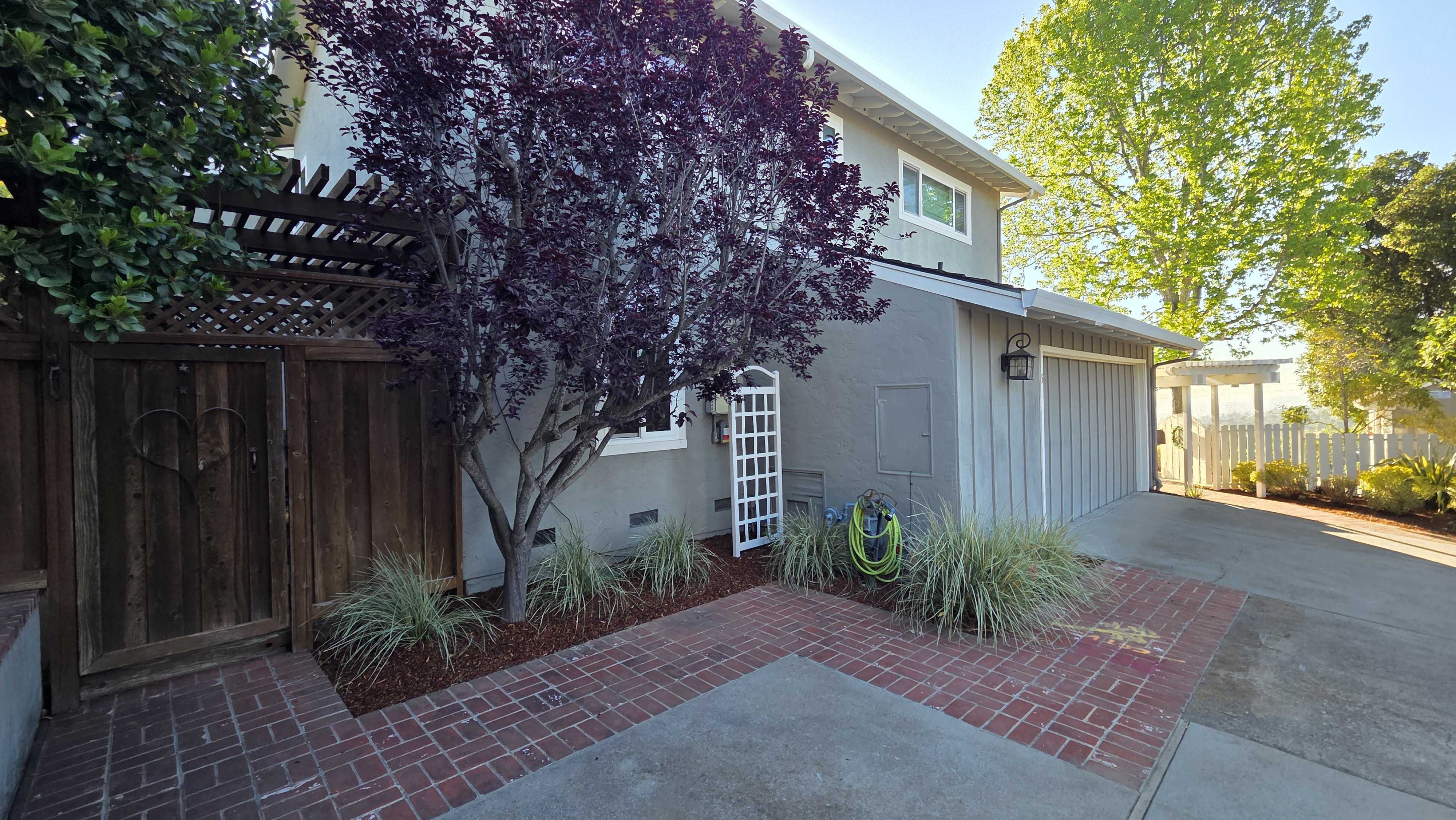 Finished paver patio and walkway adjacent to a garage and driveway. Brick interlocking pavers with a concrete inset,...