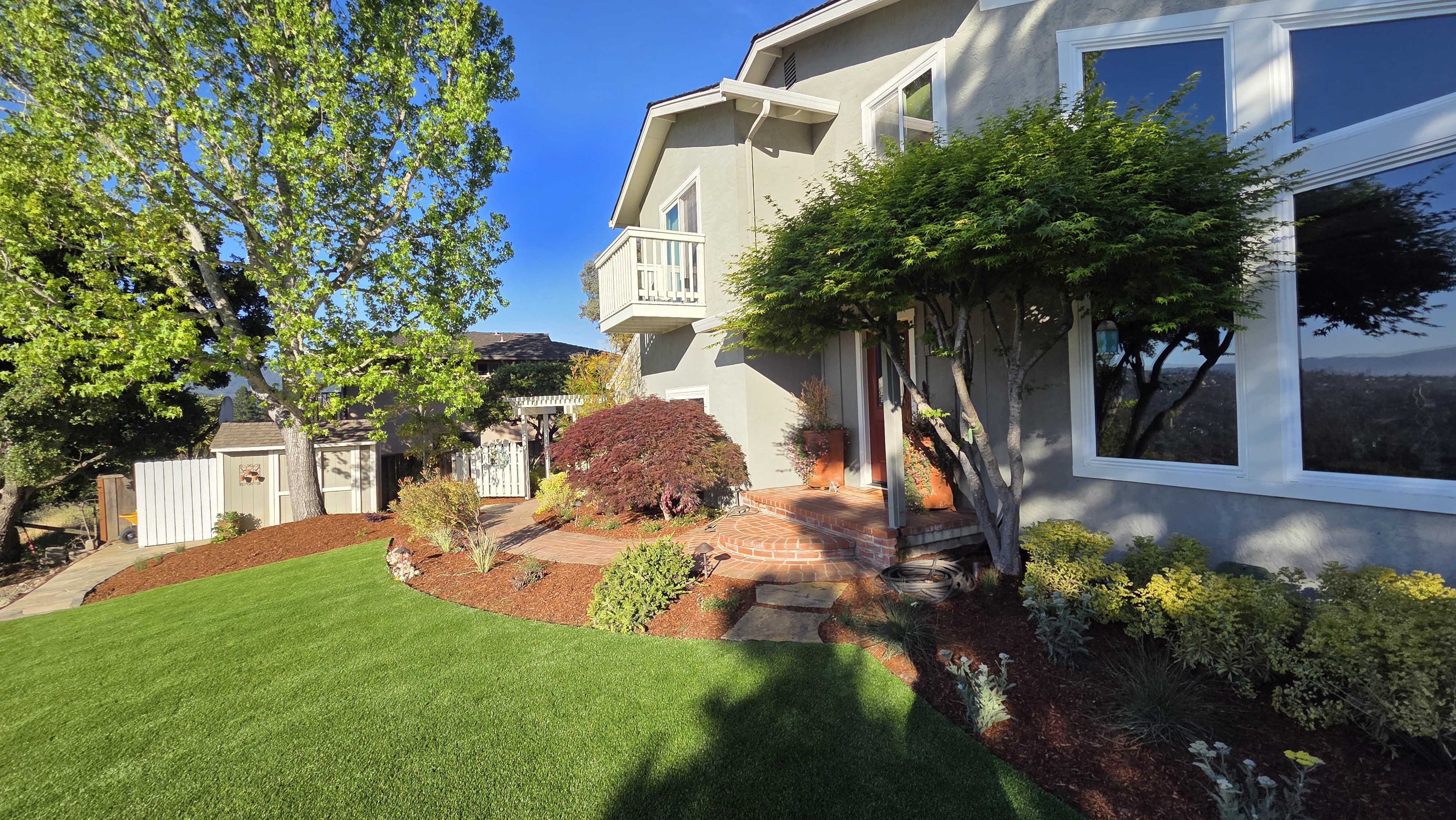Residential front/side yard showing completed artificial turf and interlocking paver walkway with steps leading to the...