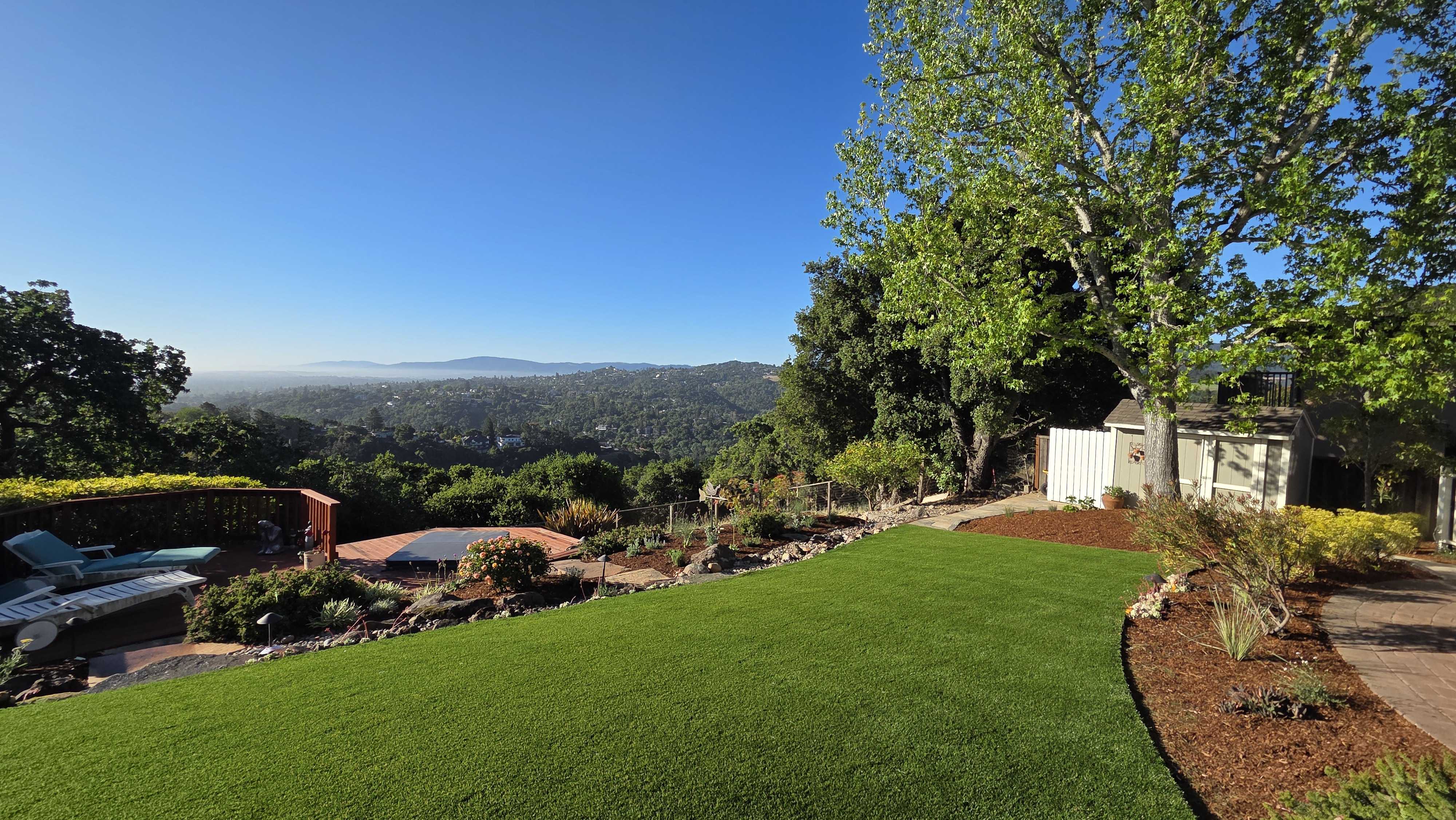 Finished backyard showing a recently installed artificial turf lawn surrounded by mulch planting beds, low segmental...