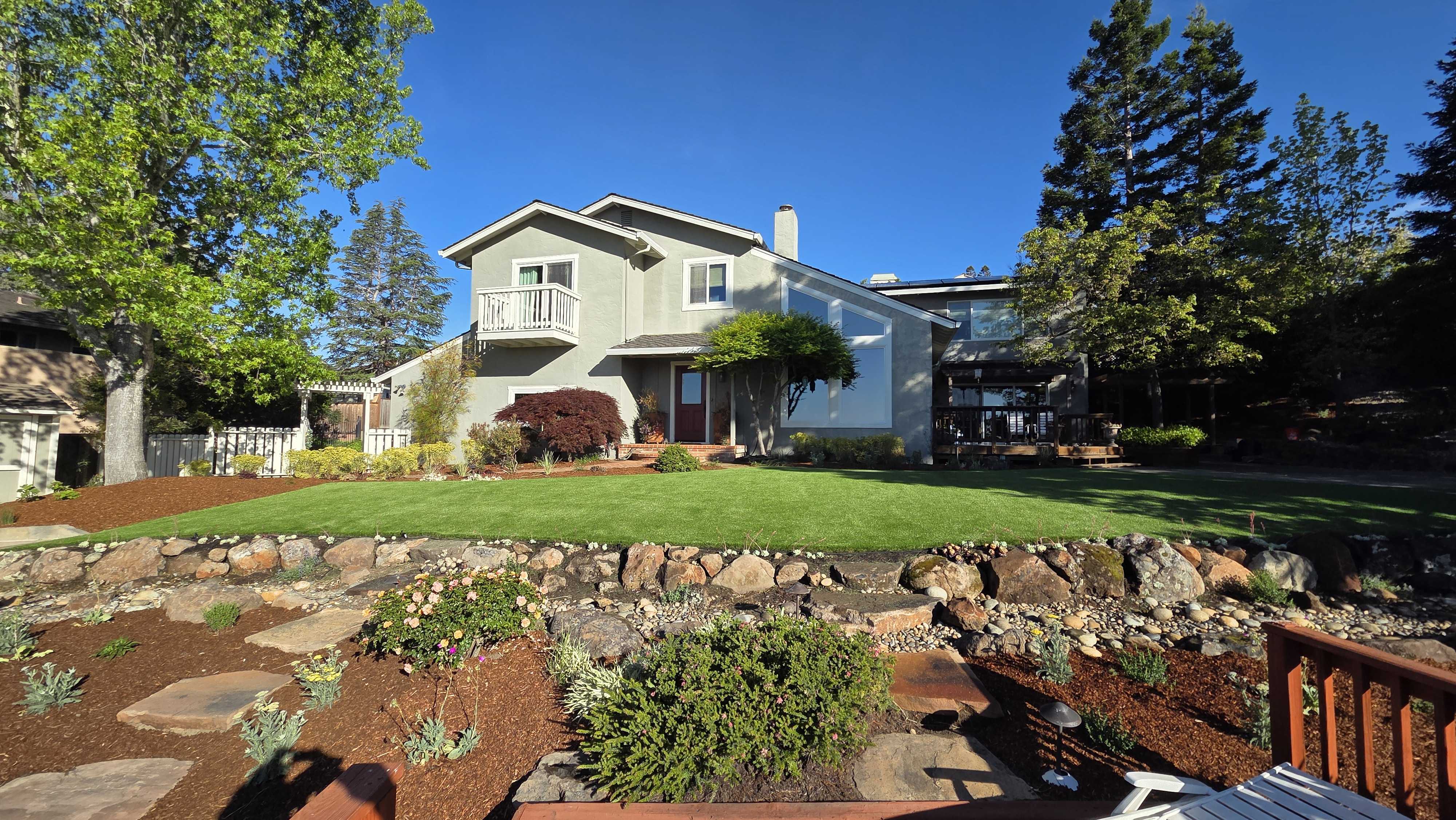 Residential backyard showing a finished sod lawn on a raised terrace behind a fieldstone retaining wall with stepping...