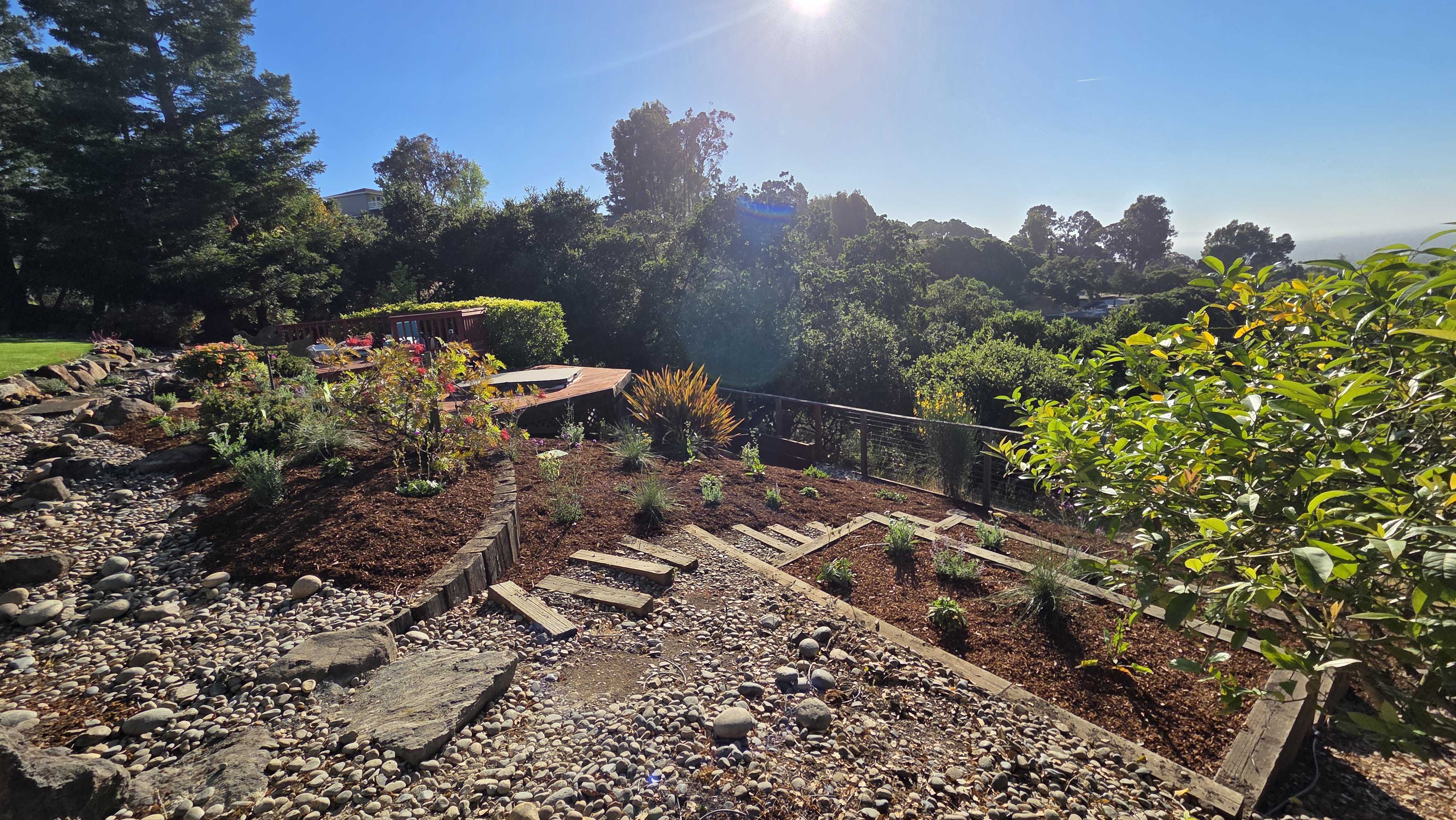 Sloped backyard showing terraced segmental retaining walls with integrated stone steps, river rock dry creek features,...