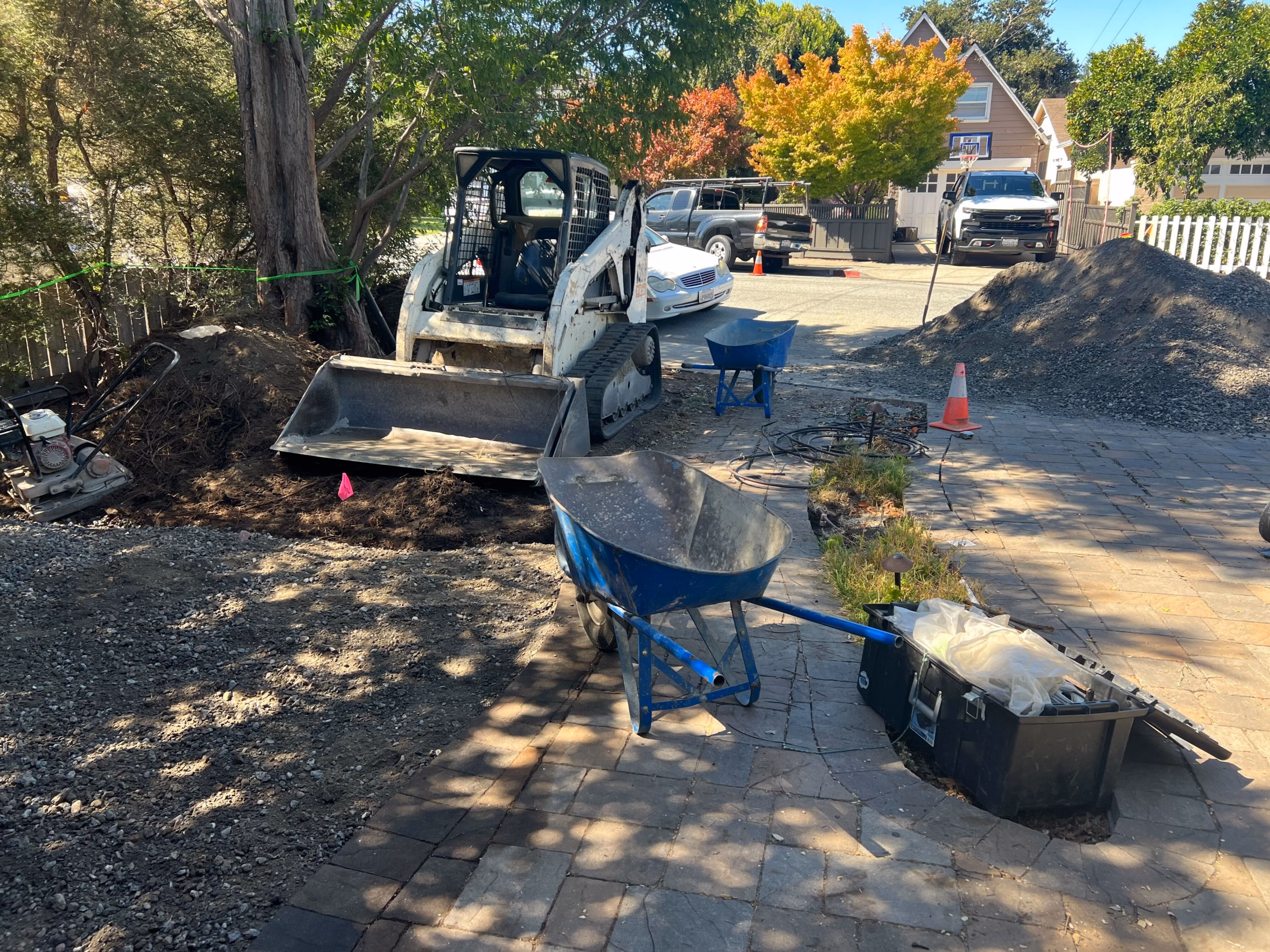Base preparation under way for the paver driveway approach, with a skid steer and aggregate base staged in San Carlos.