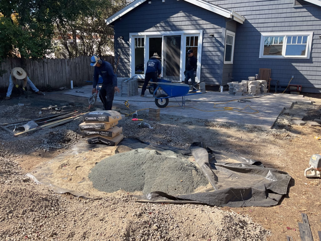 Backyard patio construction in progress with crew preparing the subbase and spreading bedding sand and crushed aggregate...
