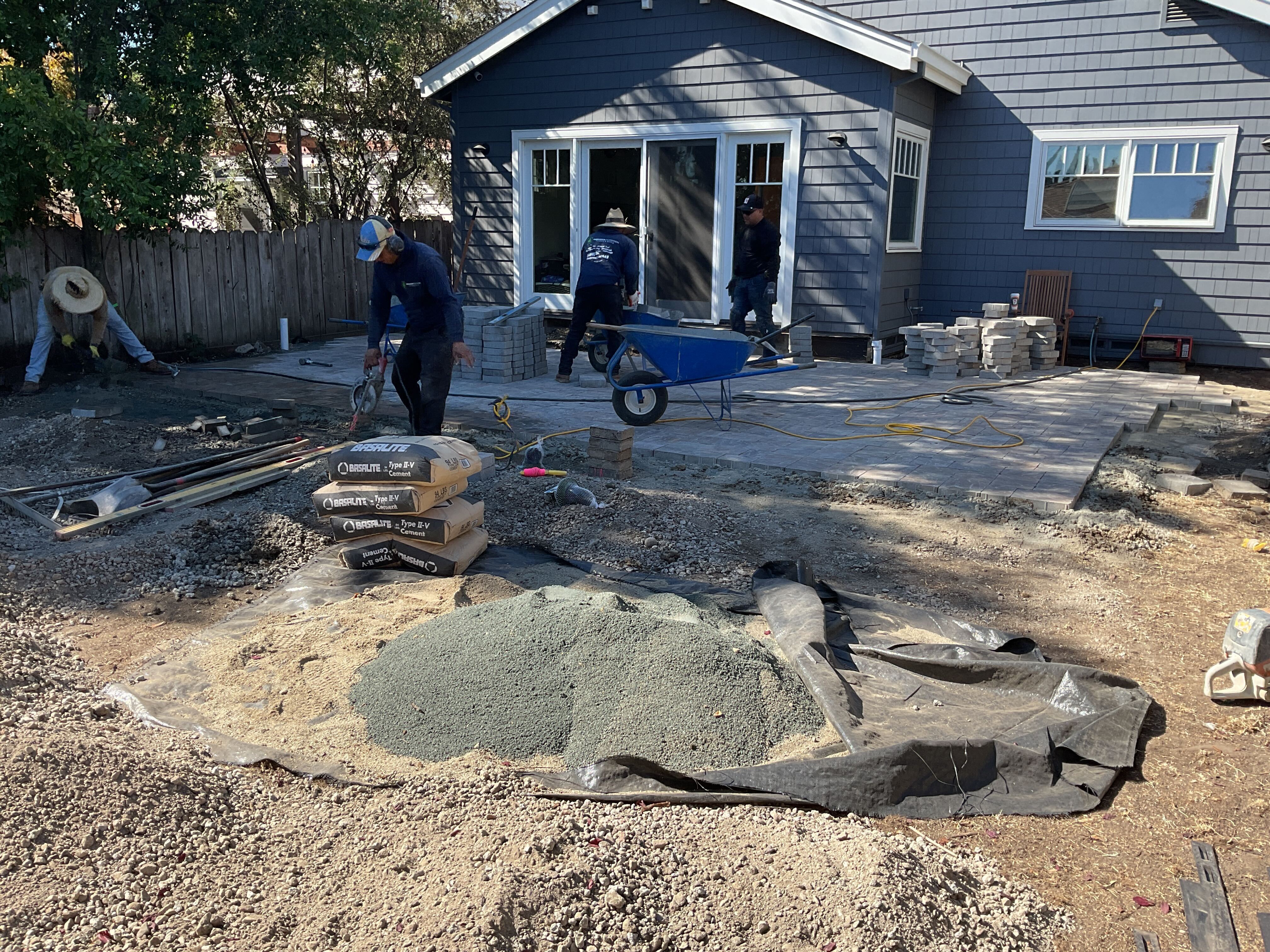 Backyard patio construction in progress with crew preparing the subbase and spreading bedding sand and crushed aggregate...