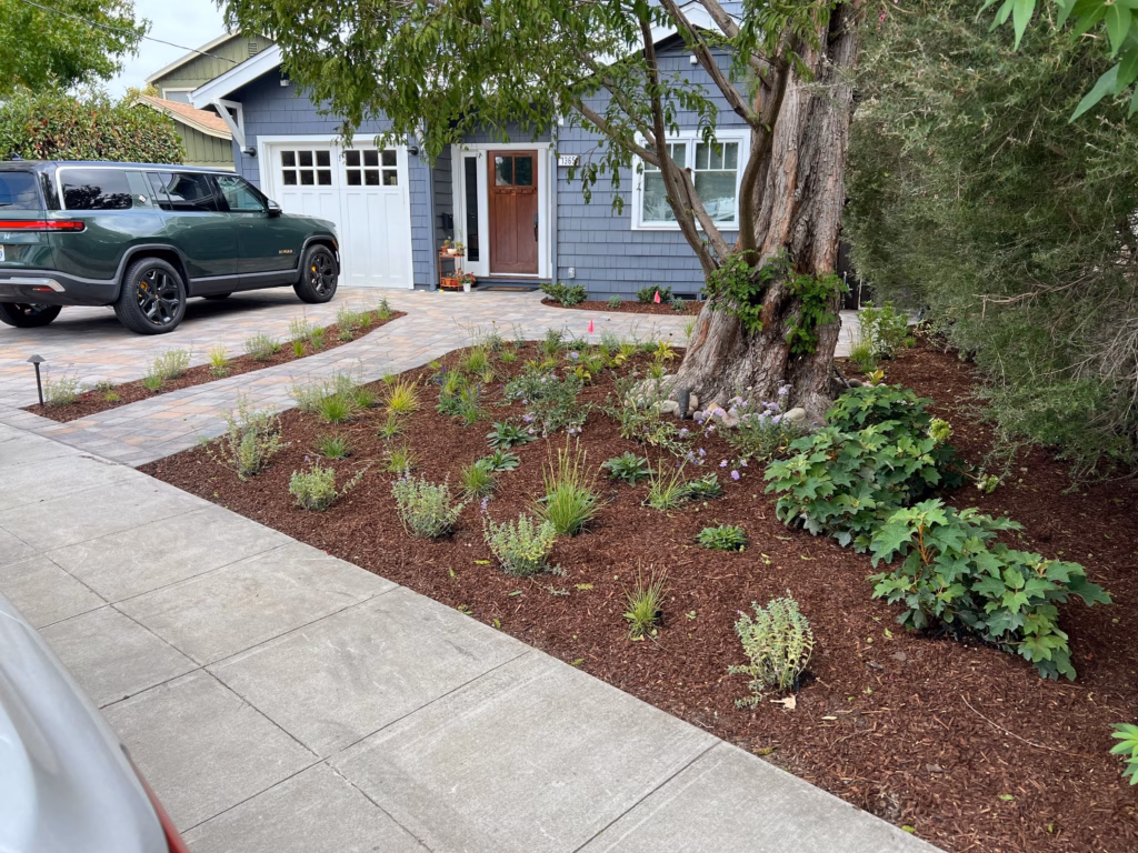Completed front-yard landscape showing an interlocking paver driveway and matching paver walkway to the home's entry,...