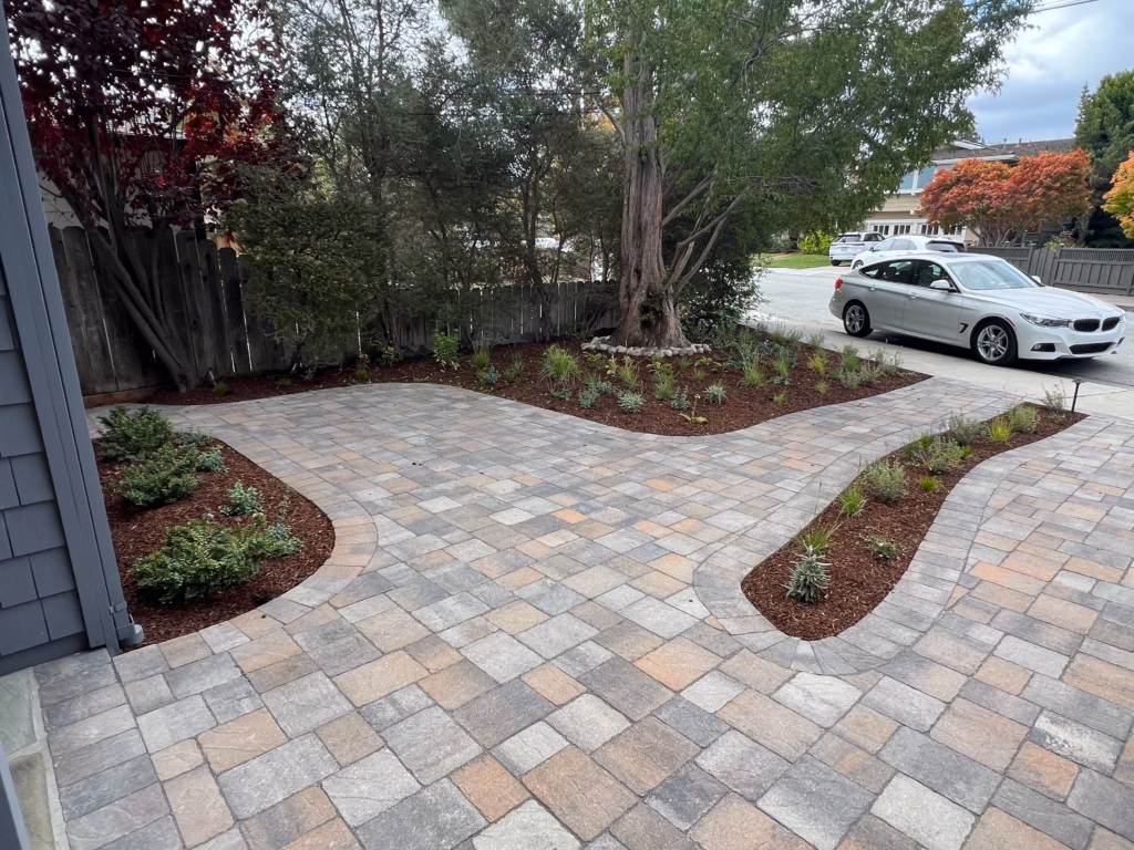Interlocking pavers installed in a mixed-size ashlar-style pattern form a new patio/drive area with clean joints. Curved...