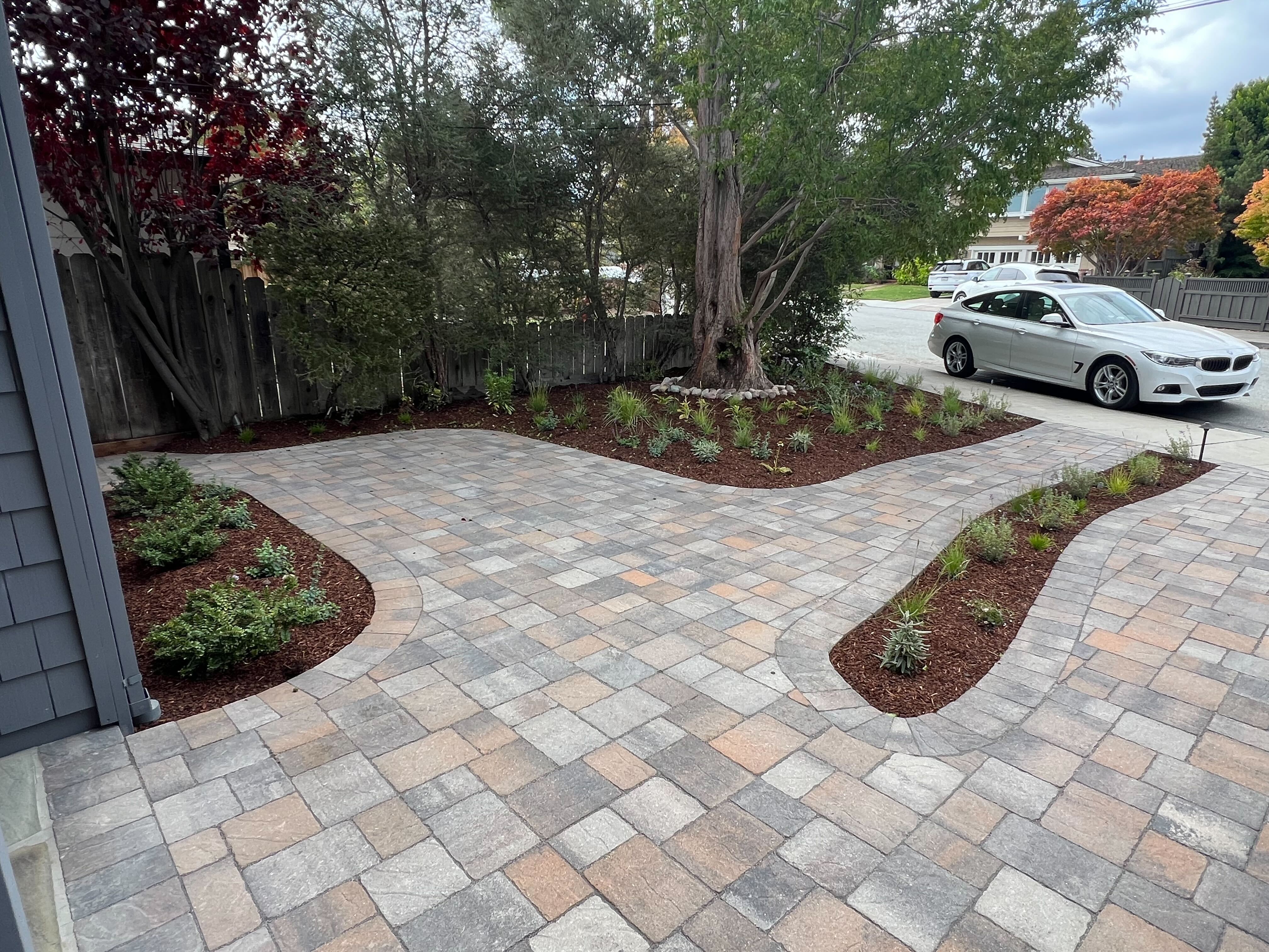 Interlocking pavers installed in a mixed-size ashlar-style pattern form a new patio/drive area with clean joints. Curved...