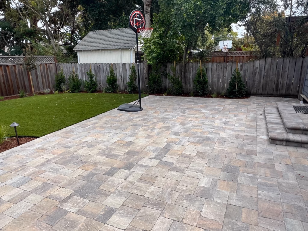 Backyard showing a newly installed interlocking paver patio in a mixed color palette with integrated steps up to the...