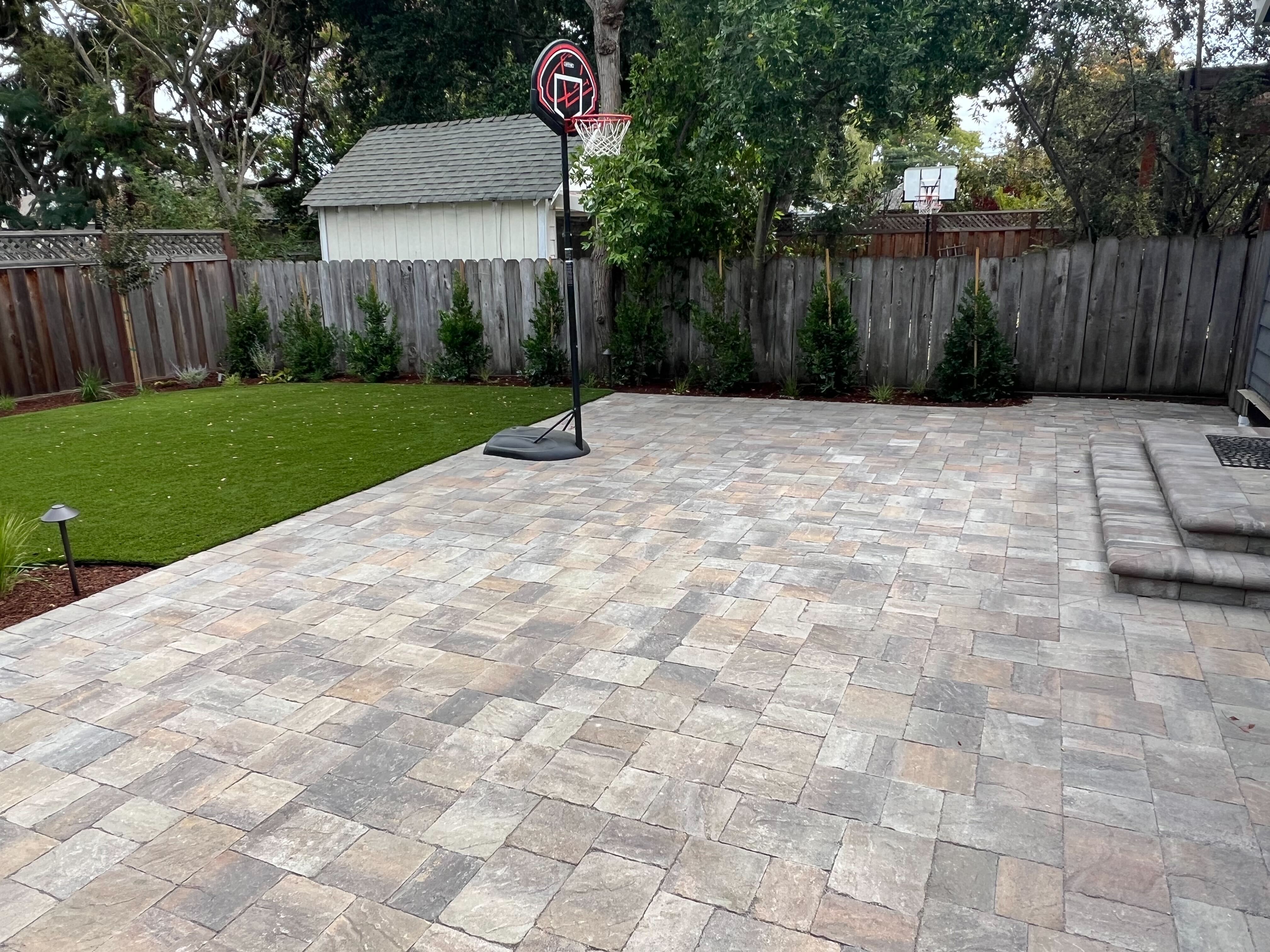 Backyard showing a newly installed interlocking paver patio in a mixed color palette with integrated steps up to the...