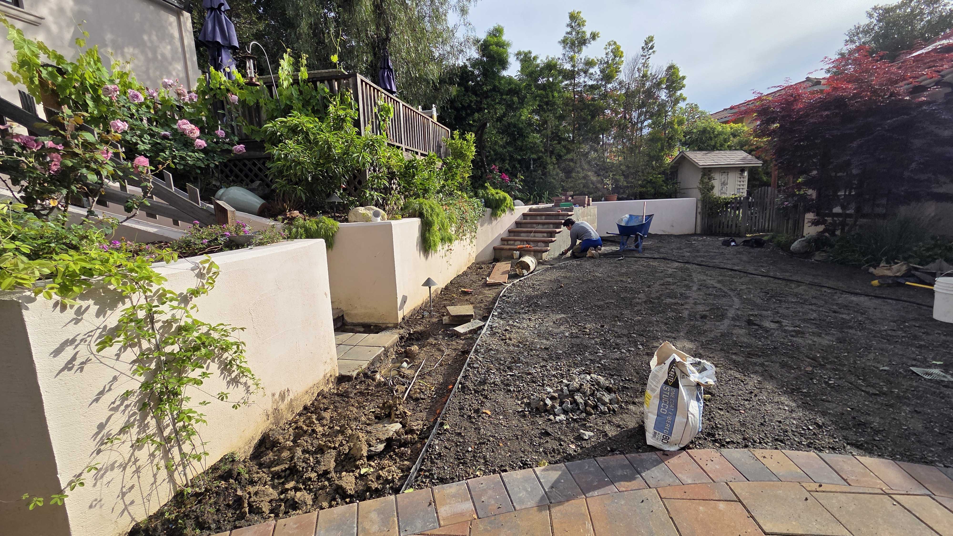 Rear yard showing a partially completed paver patio with existing interlocking pavers in the foreground and an adjacent...