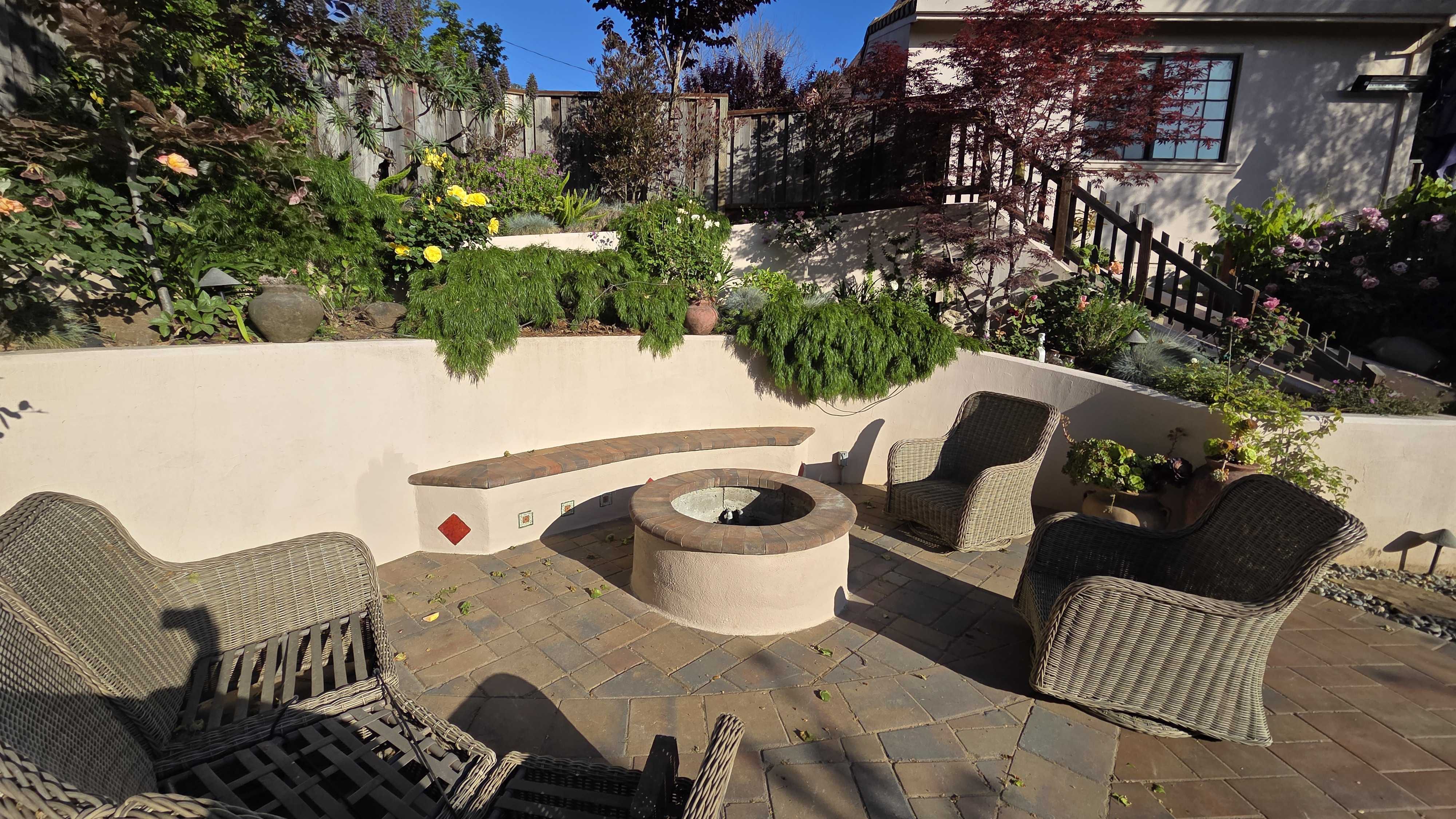 Residential backyard shows a finished interlocking paver patio with a circular fire pit and curved stucco seat/retaining...