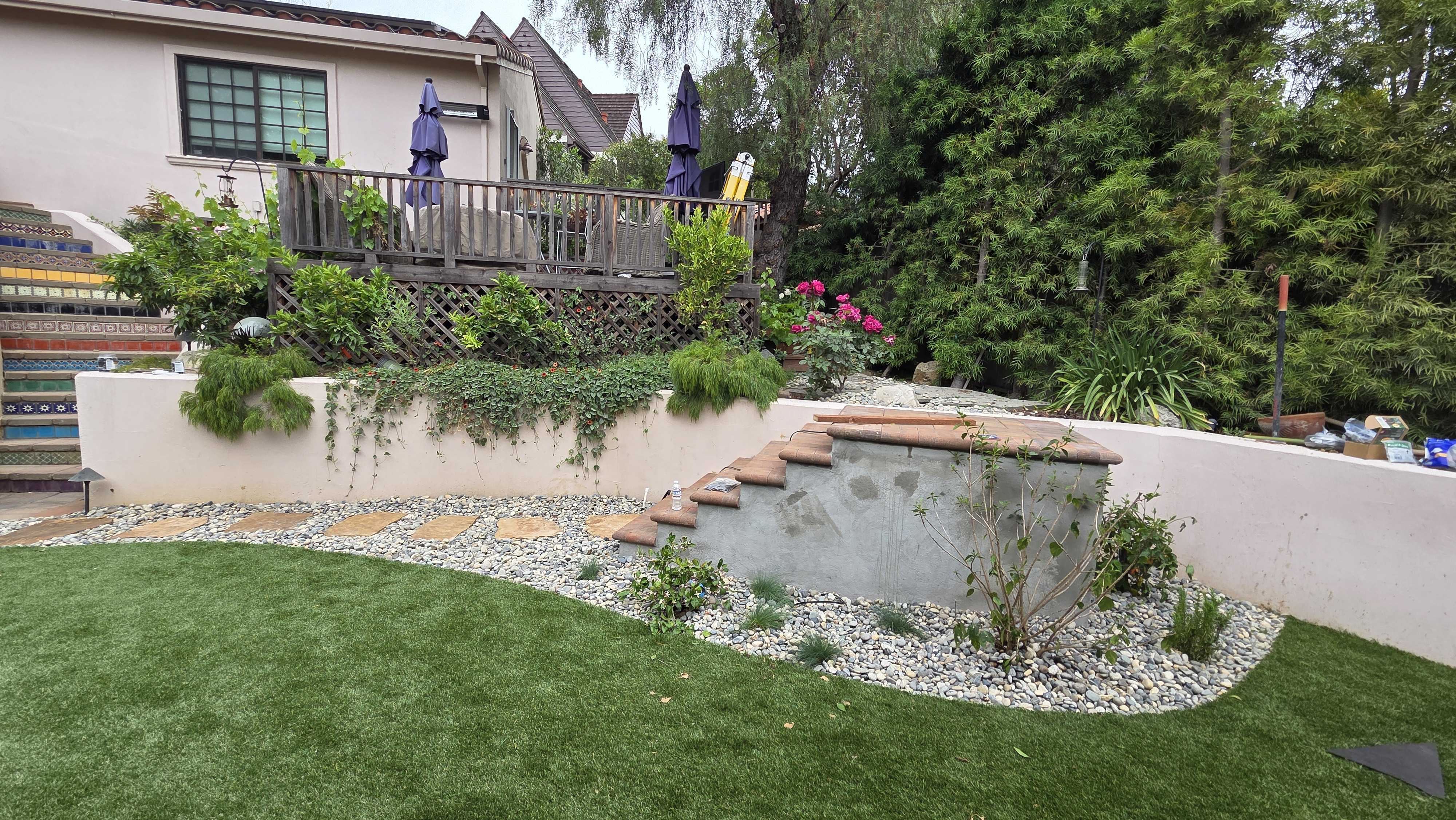 Residential backyard showing finished artificial turf with a curved edge of decorative stone and river rock. A stucco...