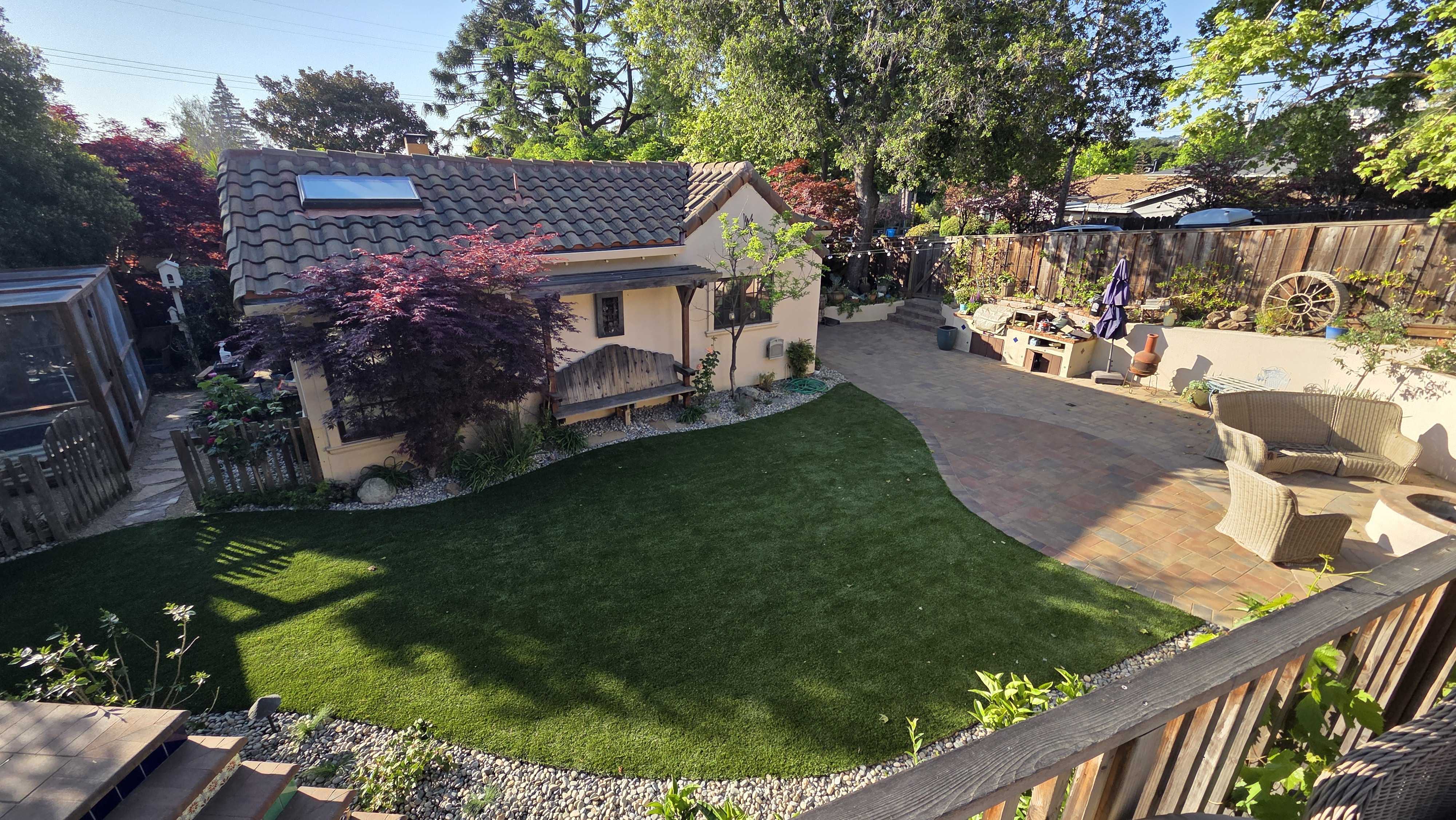 Finished backyard featuring a curved interlocking paver patio and adjoining artificial turf lawn with a low segmental...
