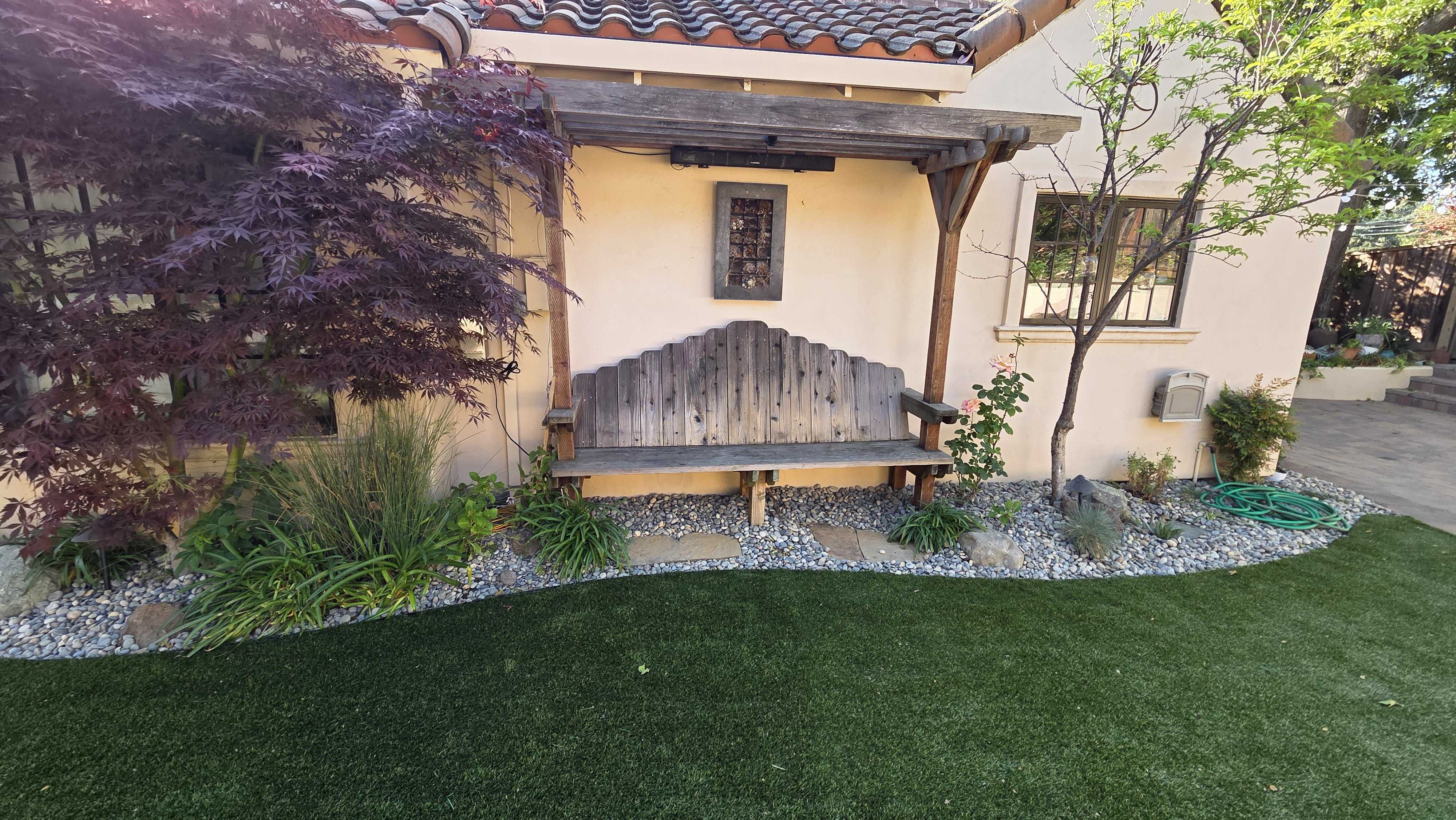 Residential backyard showing newly installed artificial turf with a clean curved edge adjacent to a river-rock planting...
