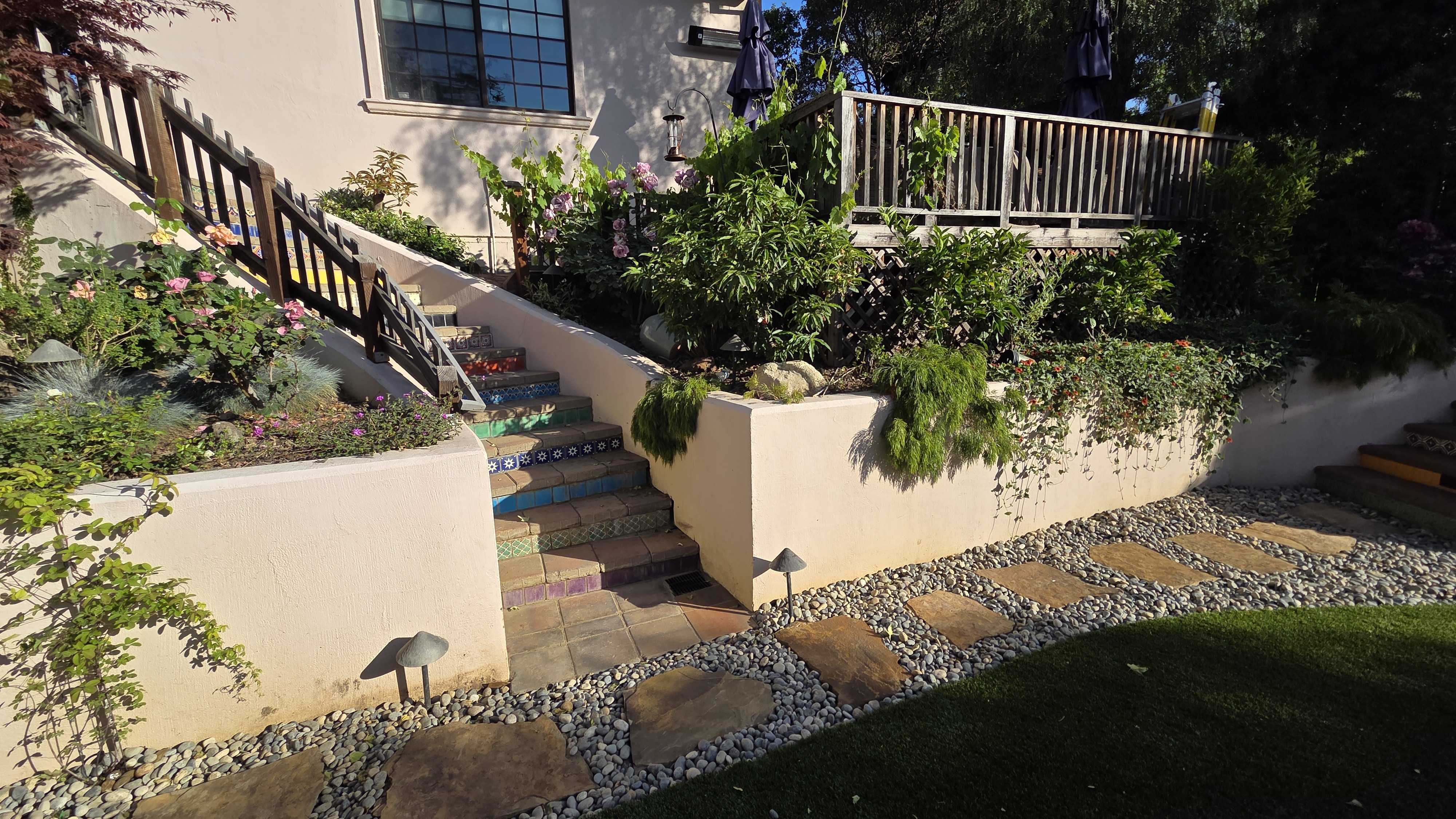 Residential backyard showing a finished hardscape with stucco retaining walls, a set of exterior stairs with decorative...