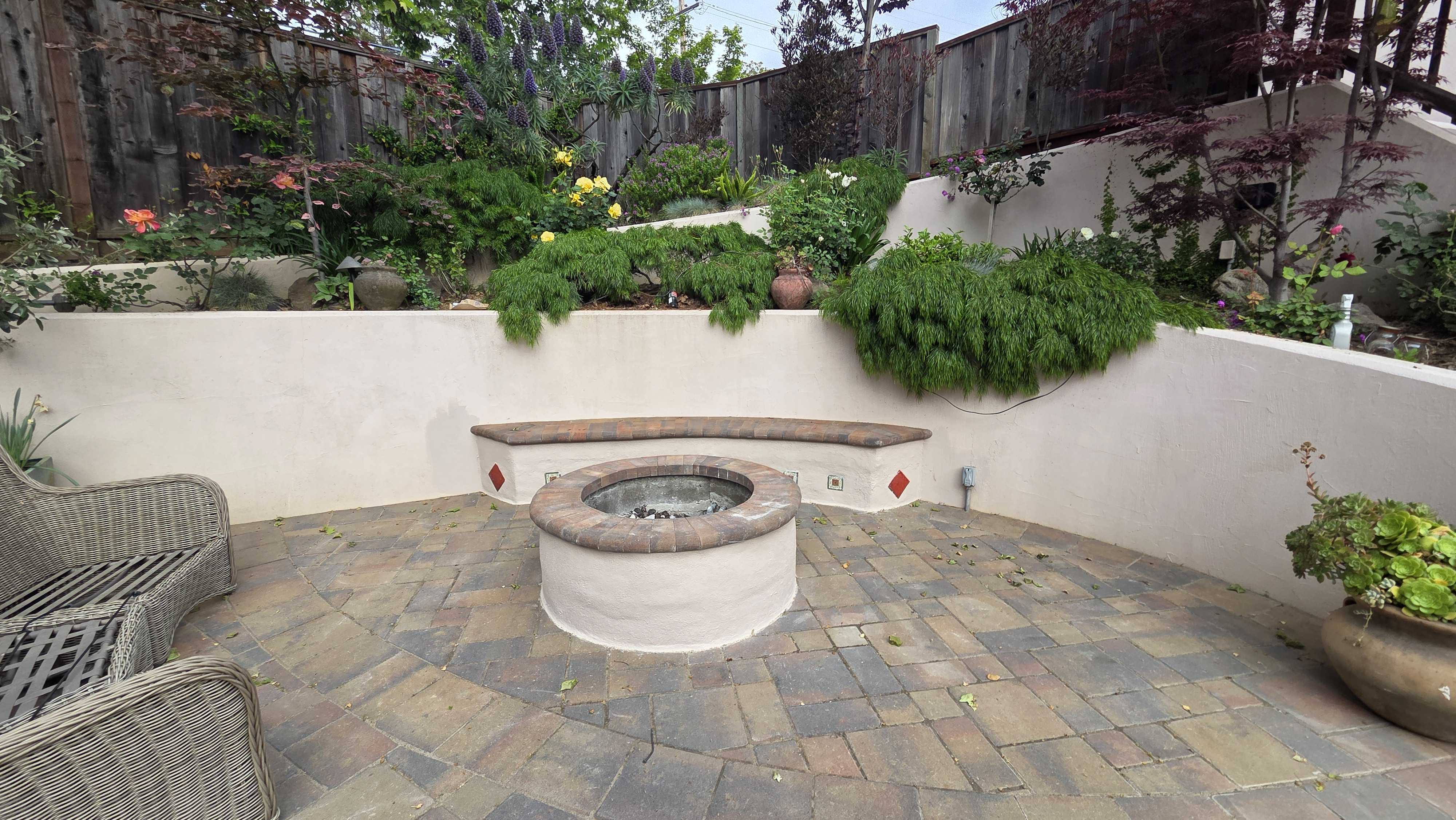 Finished residential paver patio featuring interlocking pavers in a modular pattern around a central circular raised fire...