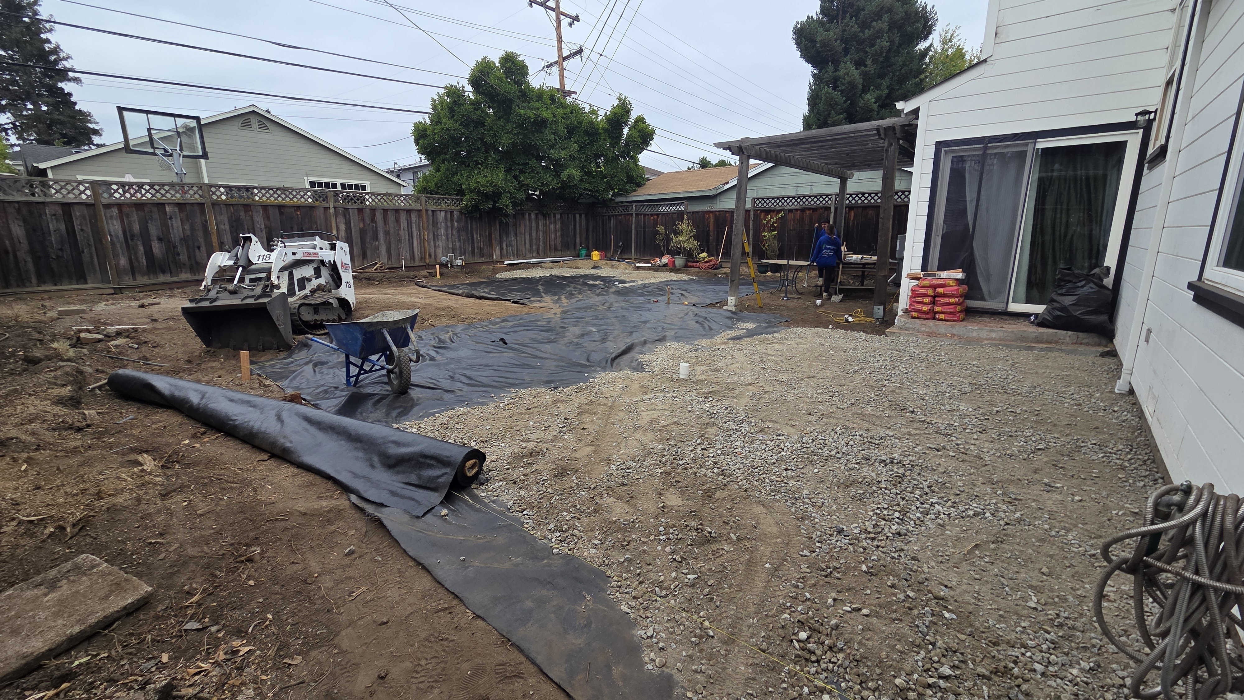 Backyard site undergoing base preparation for a patio/landscape installation; geotextile fabric is rolled out with loose...