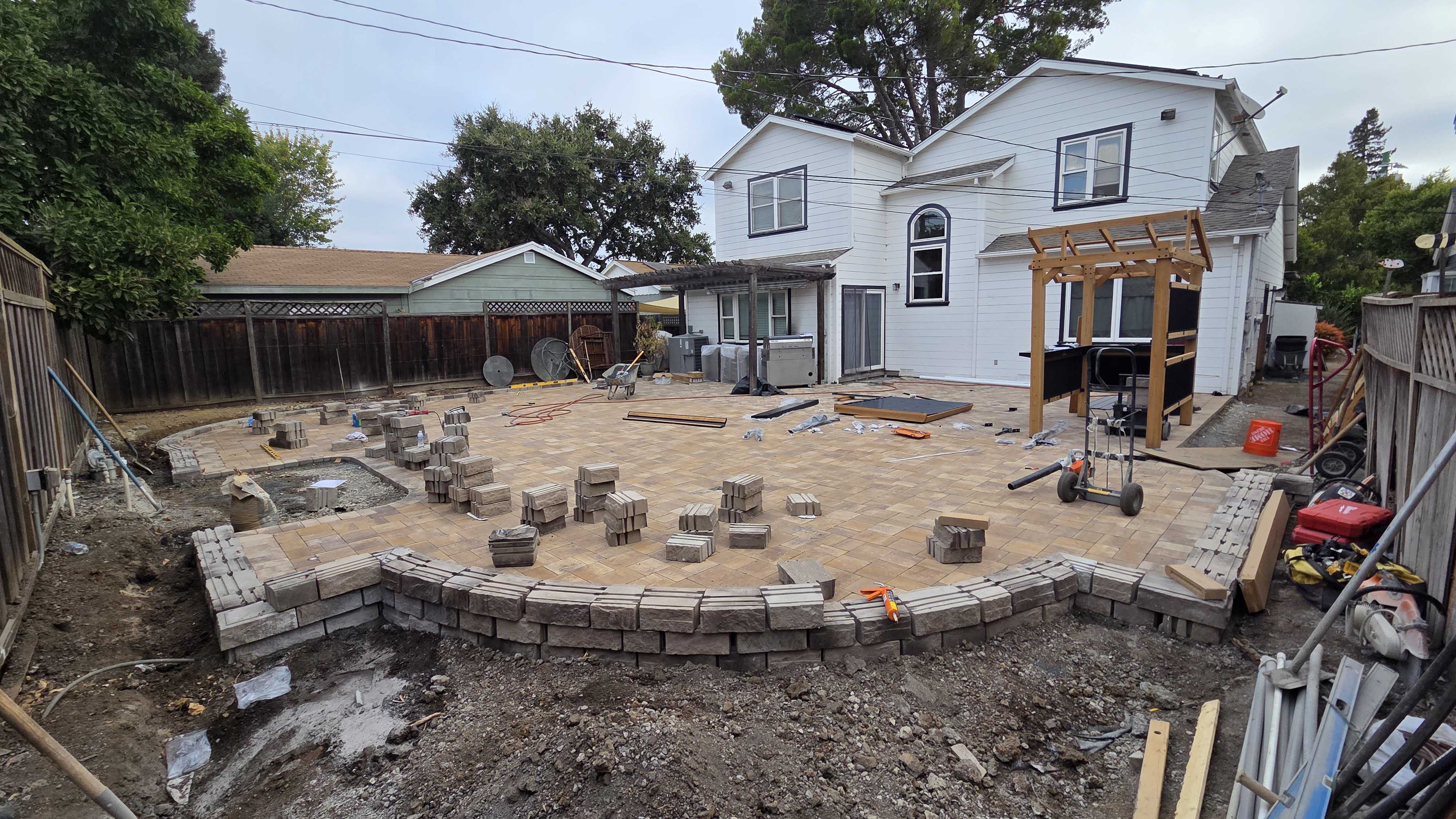 Backyard patio under active installation with interlocking pavers being set across a compacted base and a low segmental...