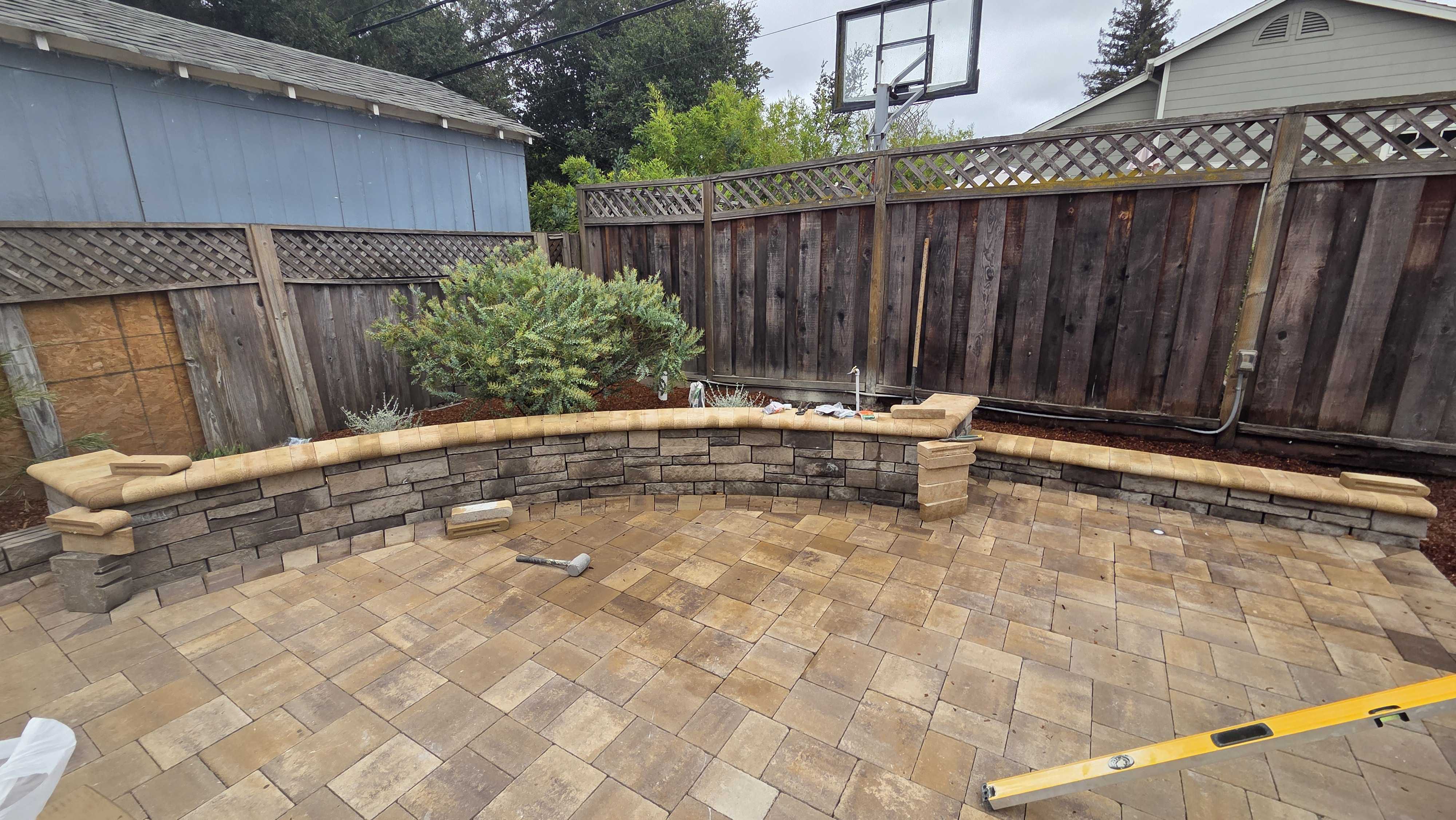 Curved segmental retaining/seating wall with capstones backs a recently laid interlocking paver patio in a residential...