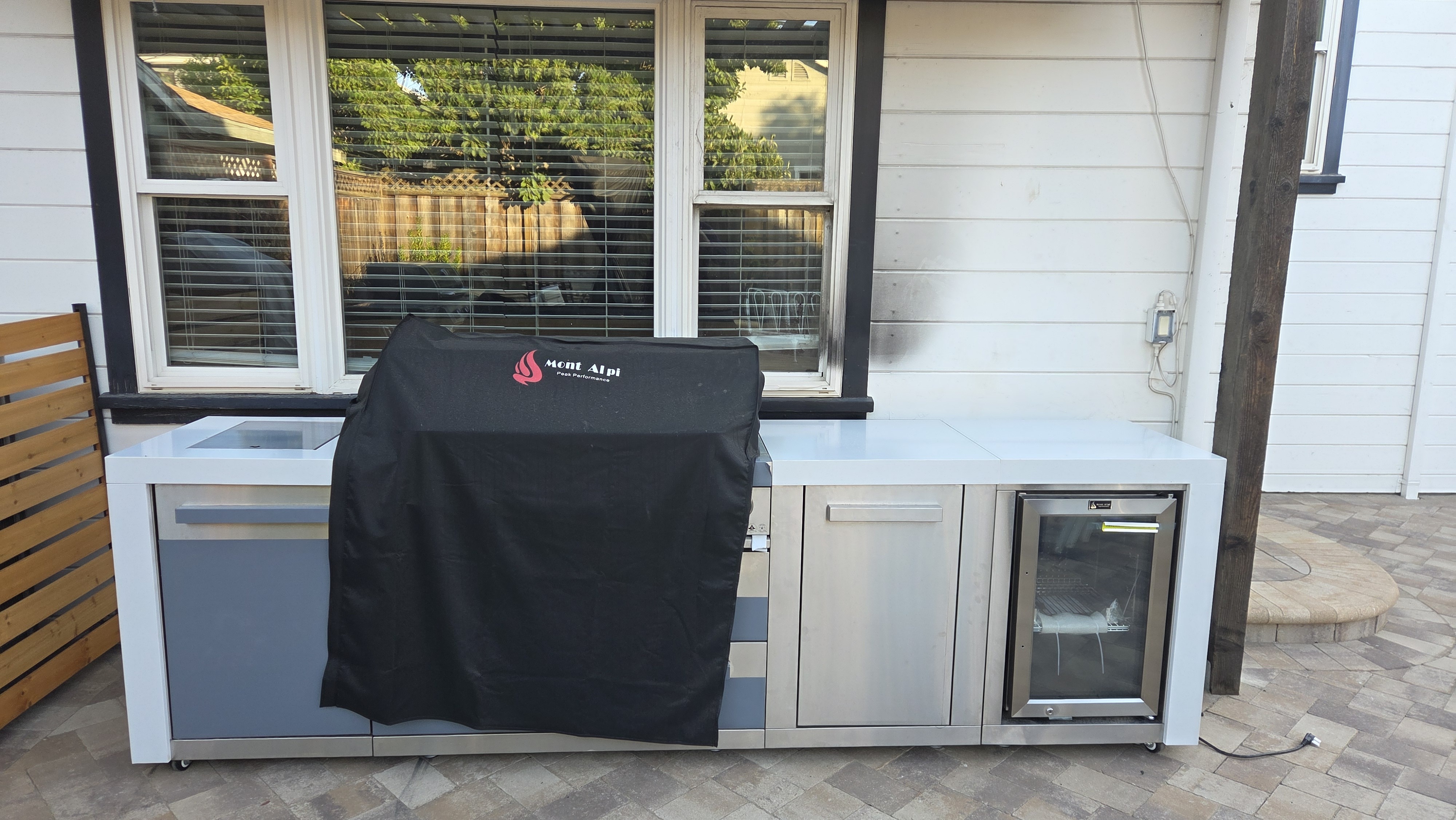 Installed outdoor kitchen run with stainless steel drawer cabinets, undercounter refrigerator, and a covered built-in...