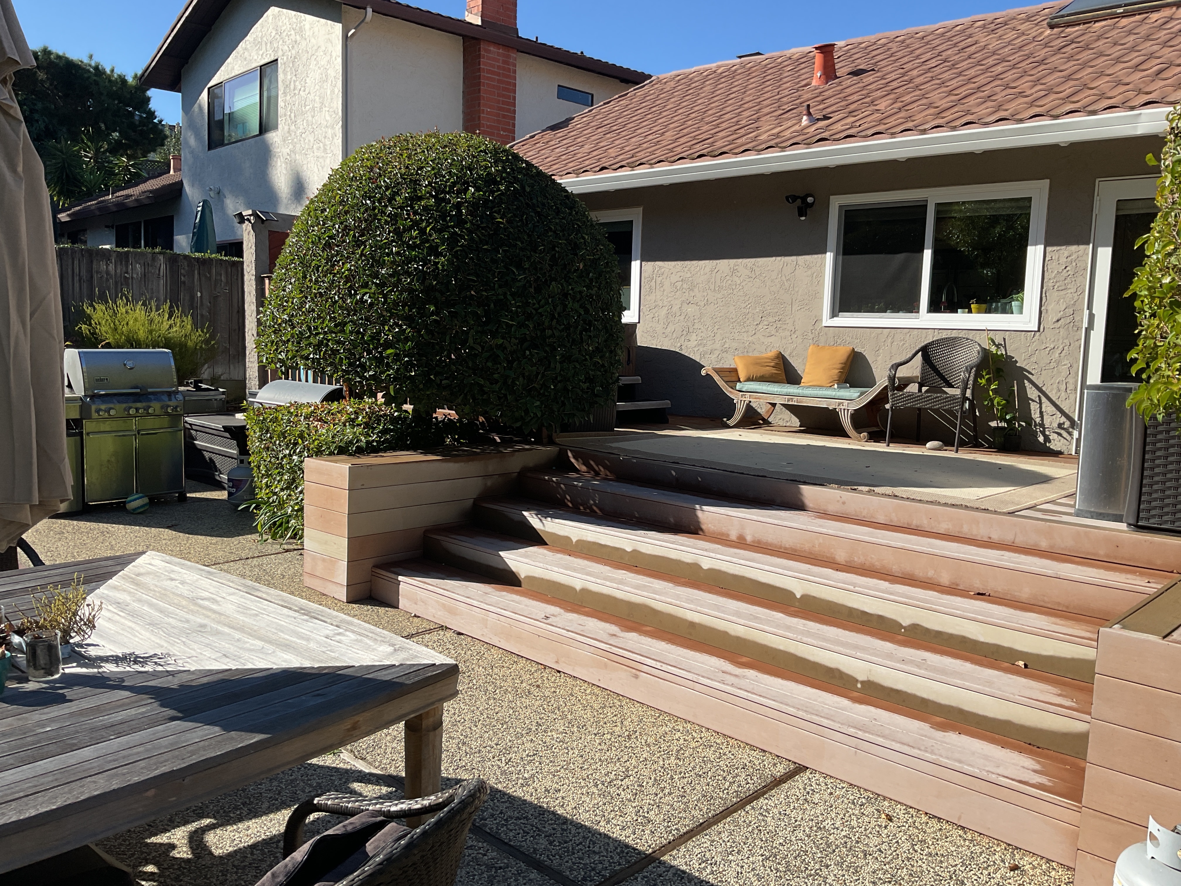 Before: narrow red-stained wood-deck step, raised wood planter, and aggregate patio at the rear elevation