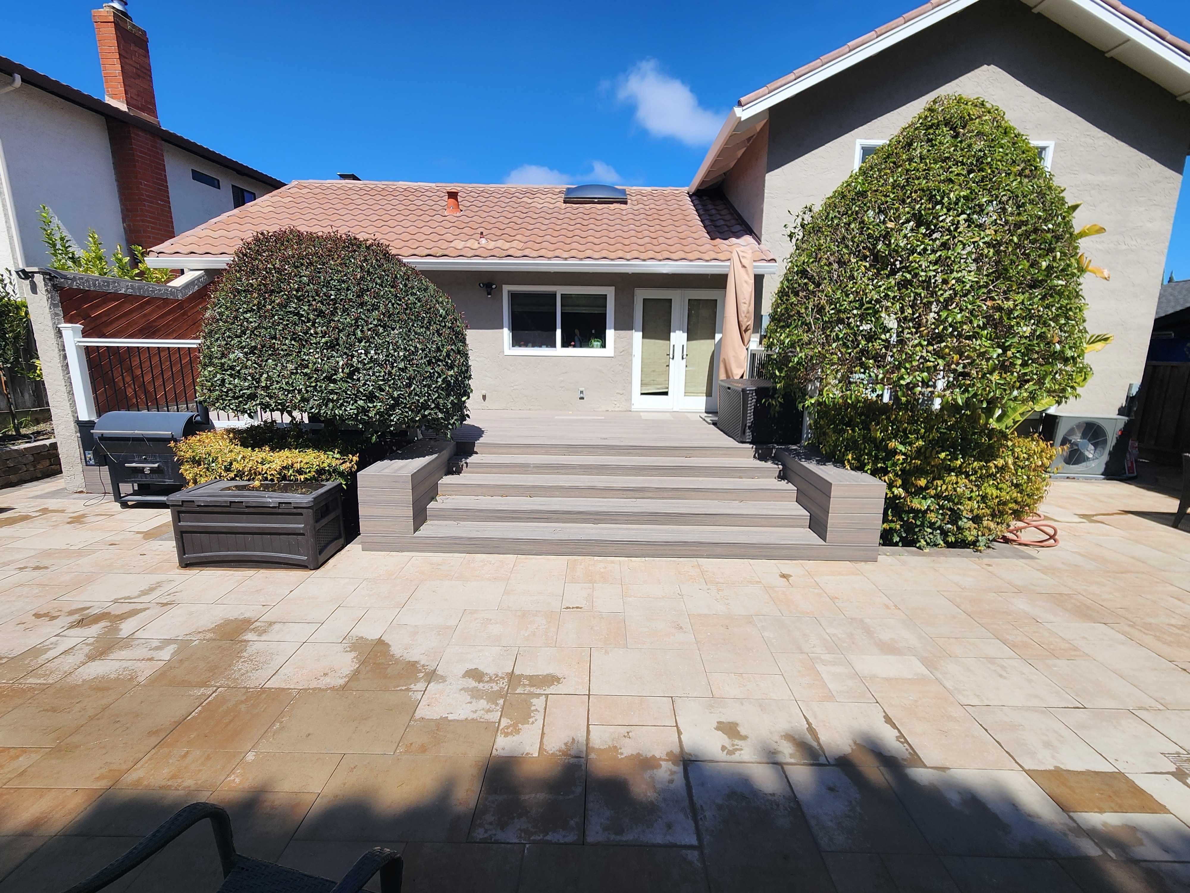 Rebuilt rear yard with a paver patio, wide composite-deck step, and symmetric topiaries along the house