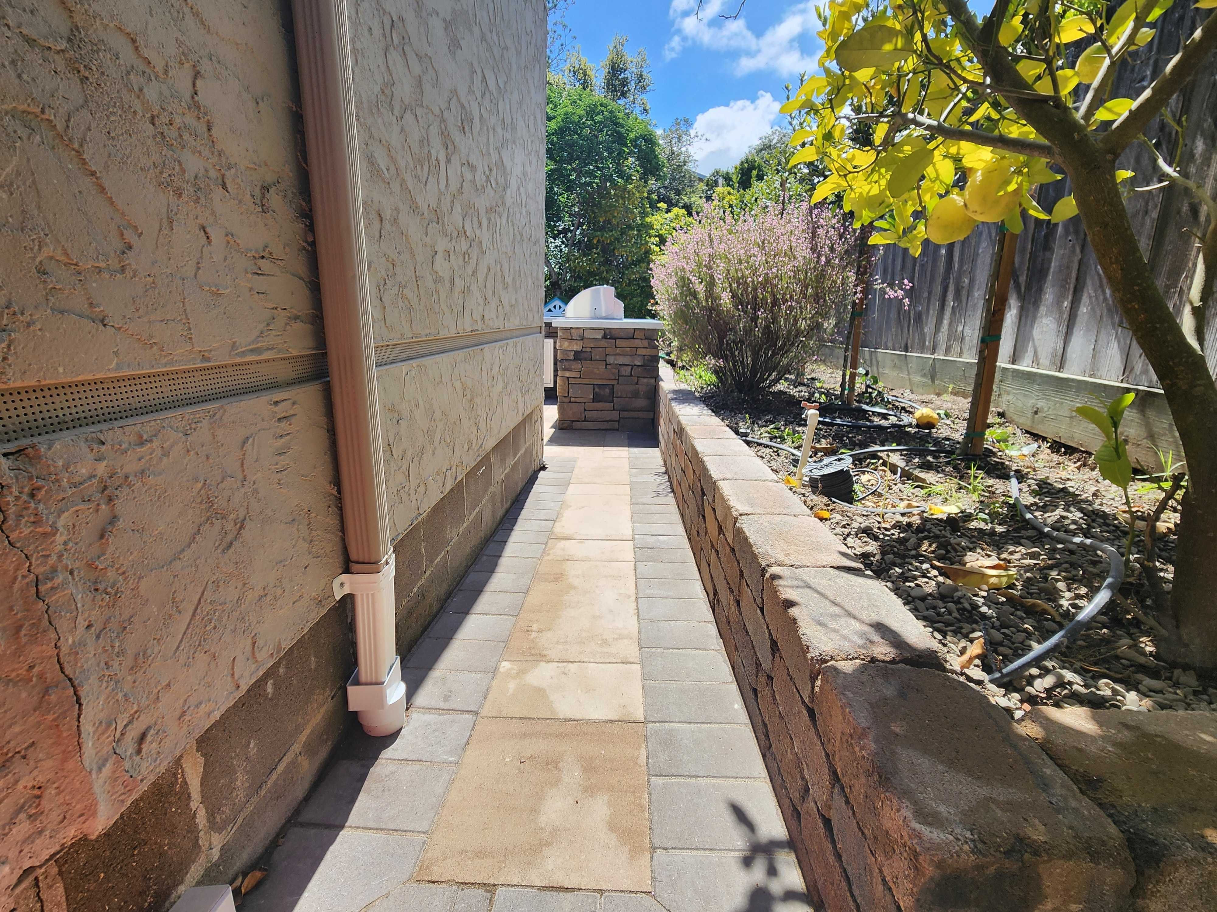 Two-tone paver walkway along a capped stone retaining wall in a landscaped side yard