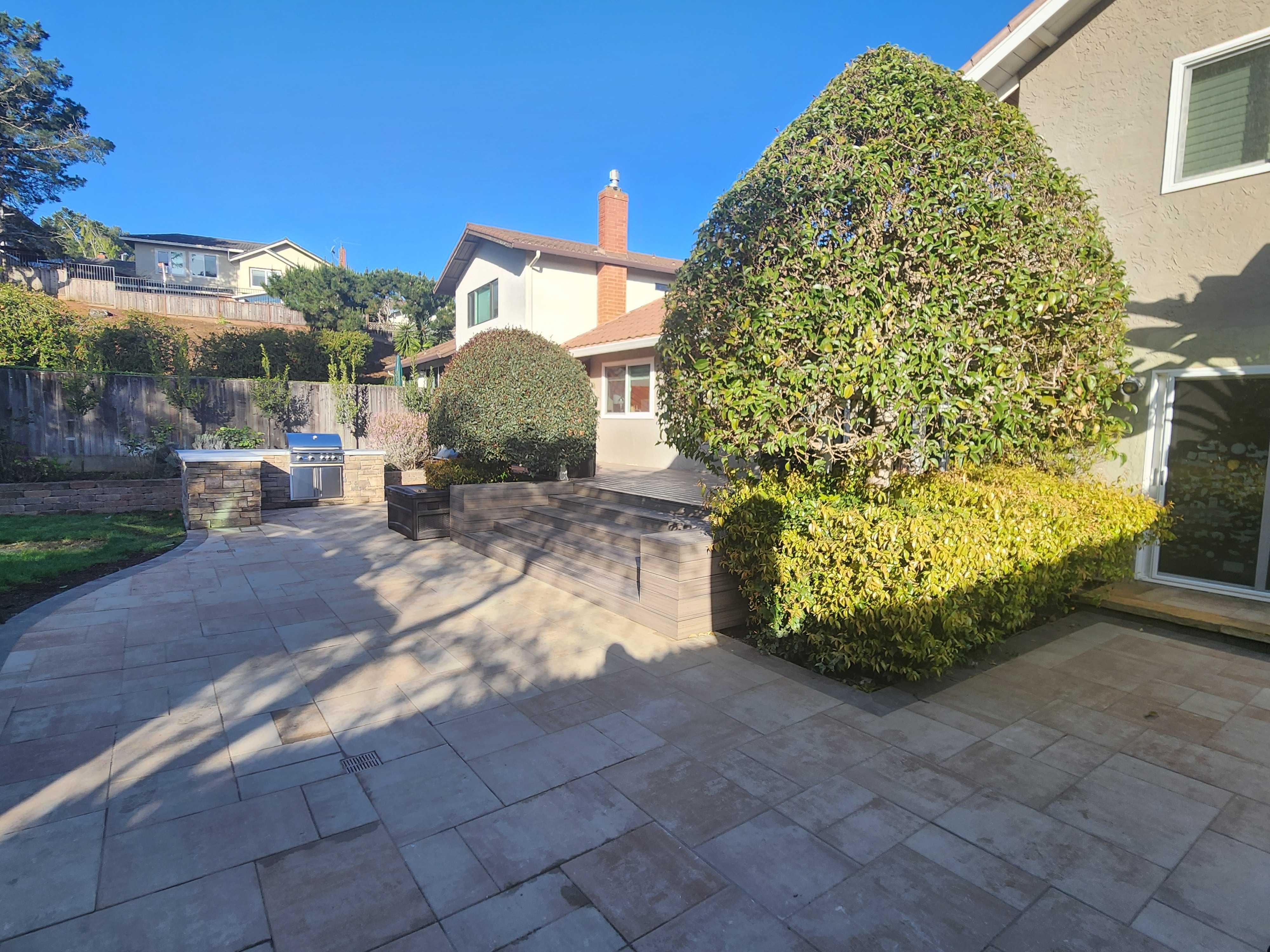Finished large-format paver patio with the stone outdoor kitchen at rear and a wide composite-deck step