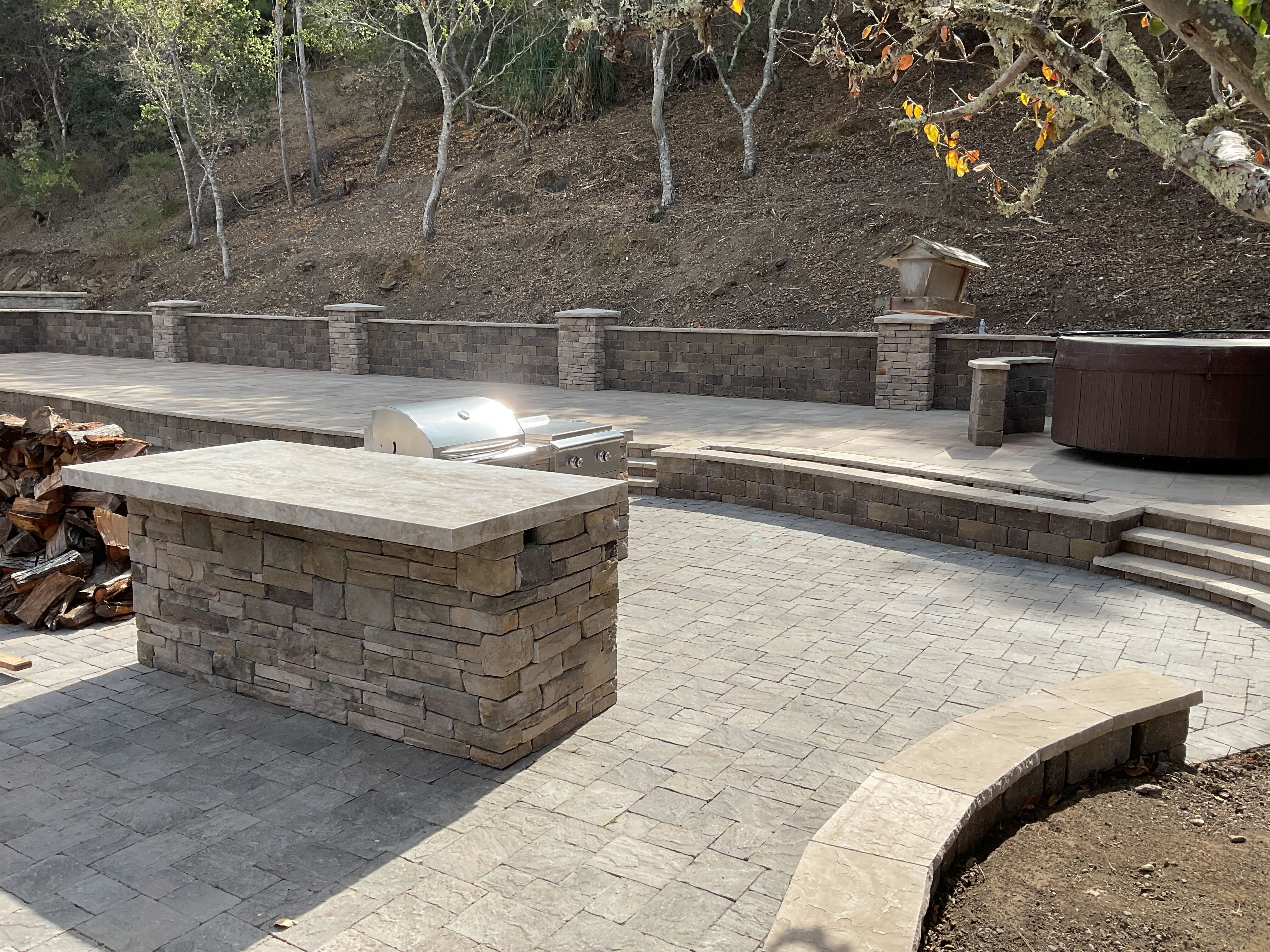 Wide backyard view with paver patio, stone-veneer retaining wall, capped pillars, outdoor kitchen island and hot tub...