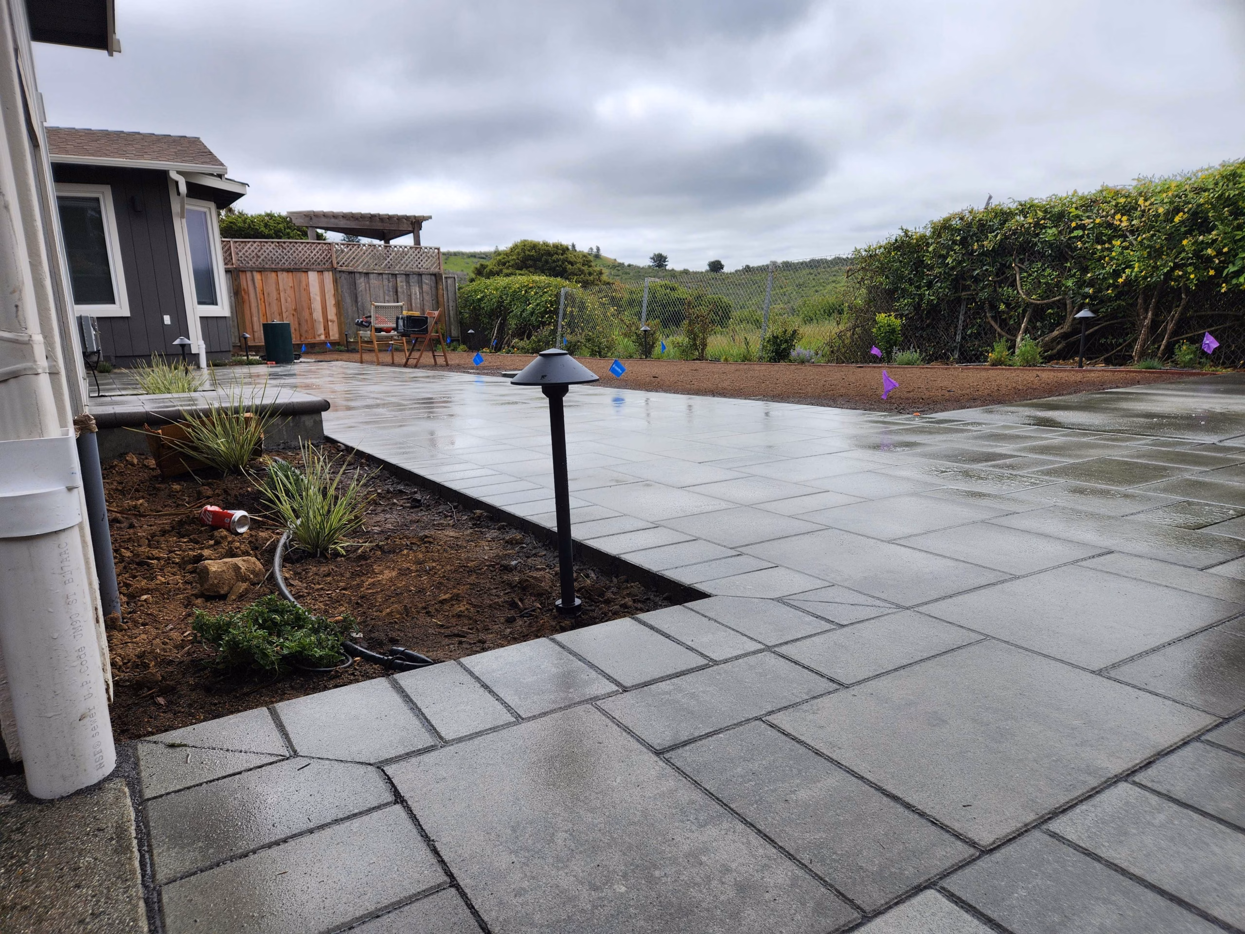A large-format light-gray paver patio with a charcoal border band, a planted gravel strip and a path light along a wood fence, in Mountain View