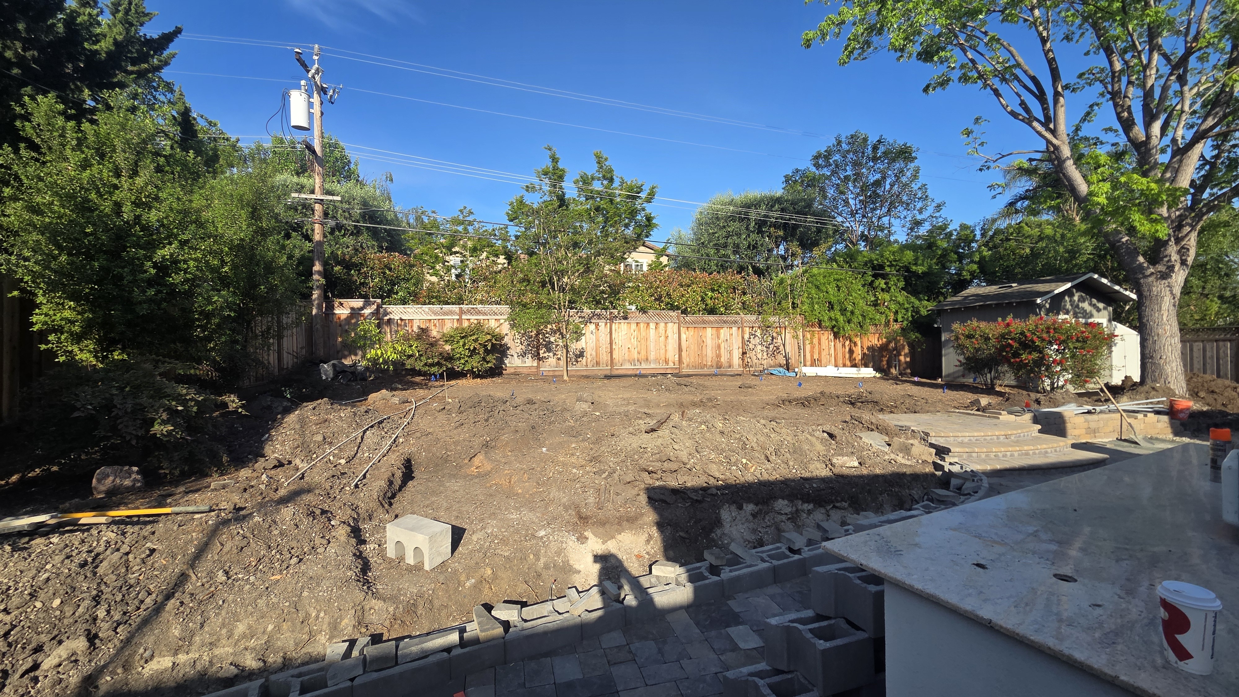 Wide view of the cleared and graded bare-dirt backyard before landscaping, with staged blocks and the edge of the kitchen...