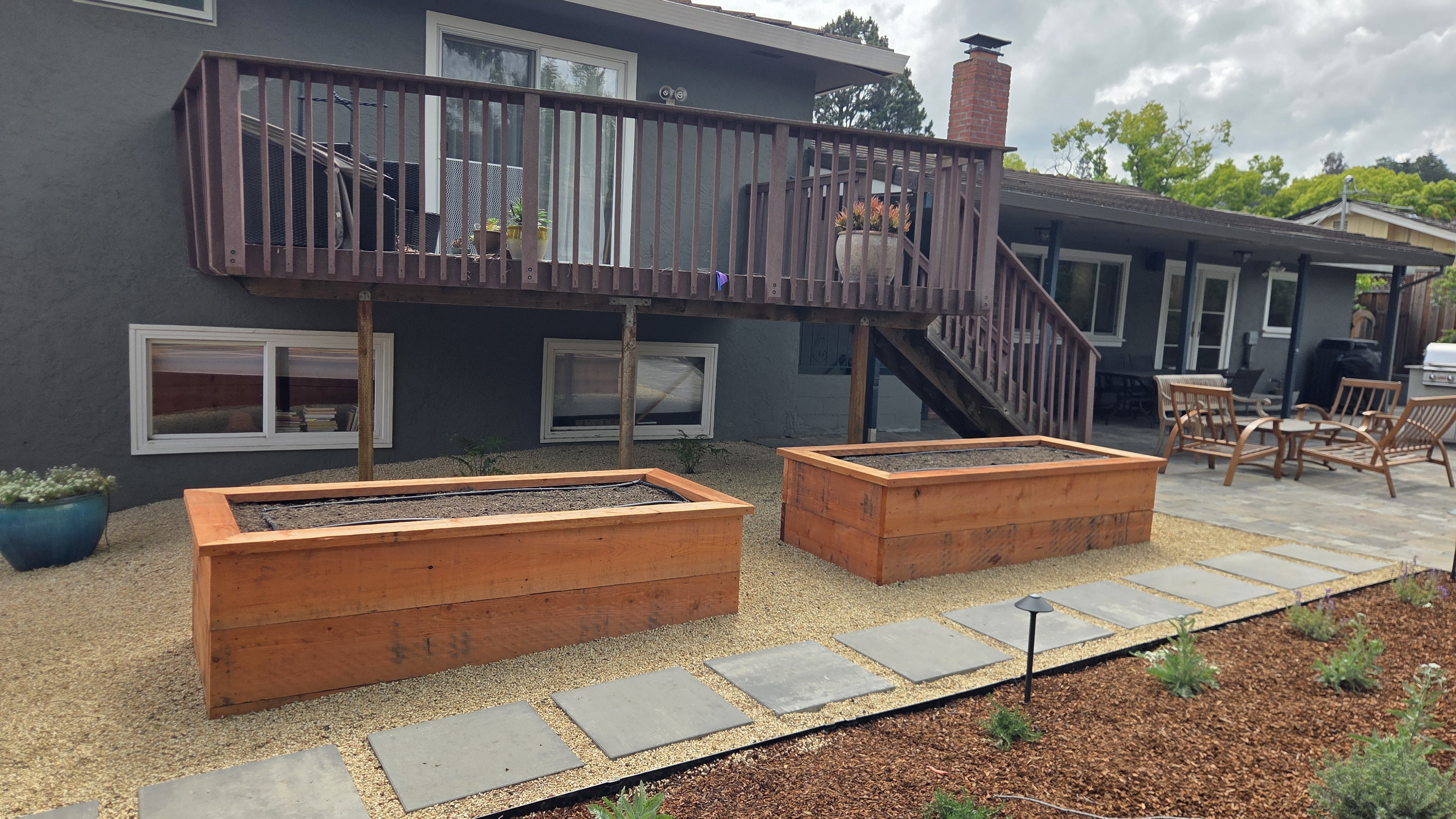 Finished landscape view of two new redwood raised garden beds flanking a bluestone stepping-stone path against the rear...