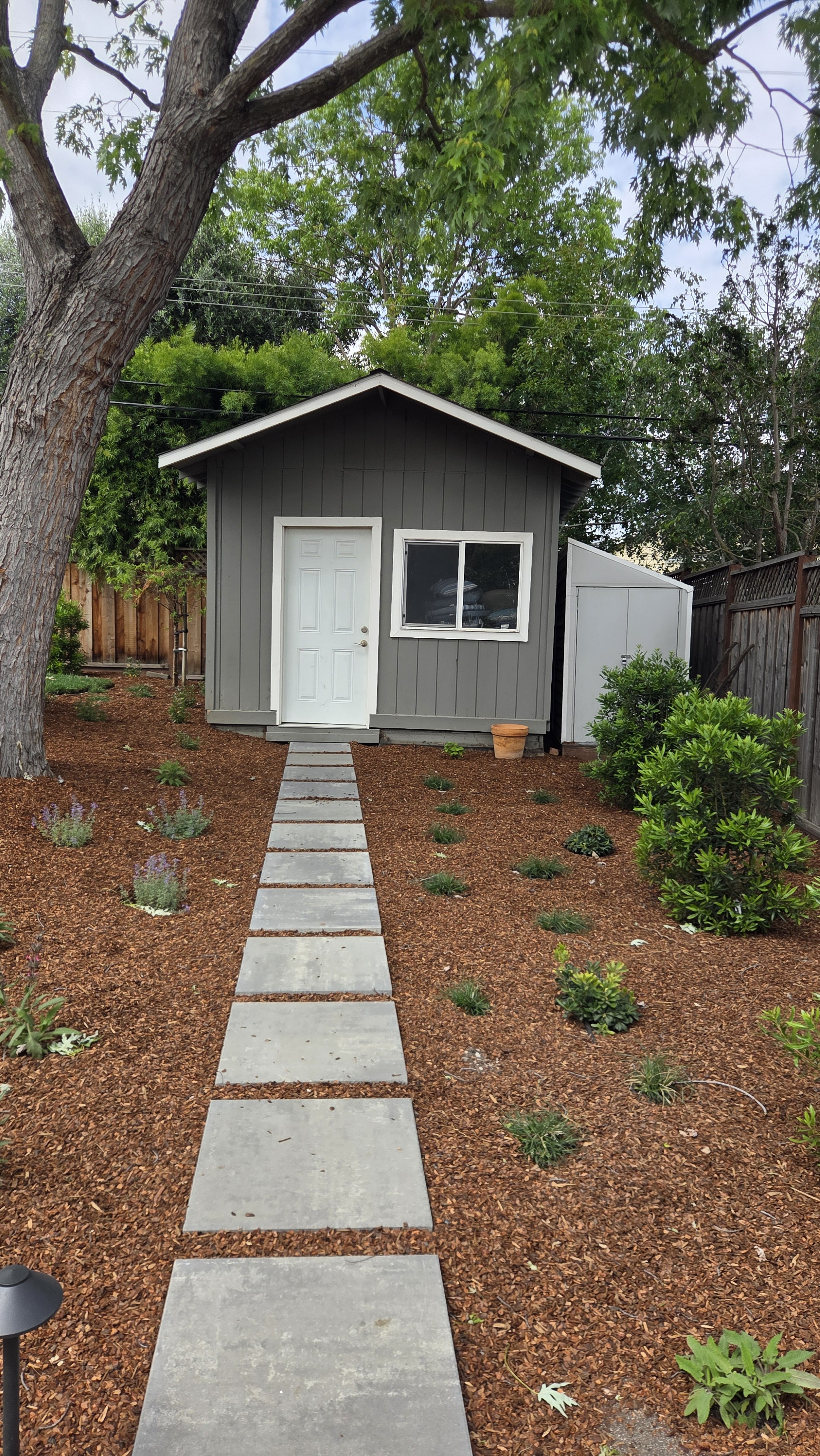 A symmetrical concrete-paver stepping-stone walkway runs through fresh mulch beds with new plantings up to a grey garden...