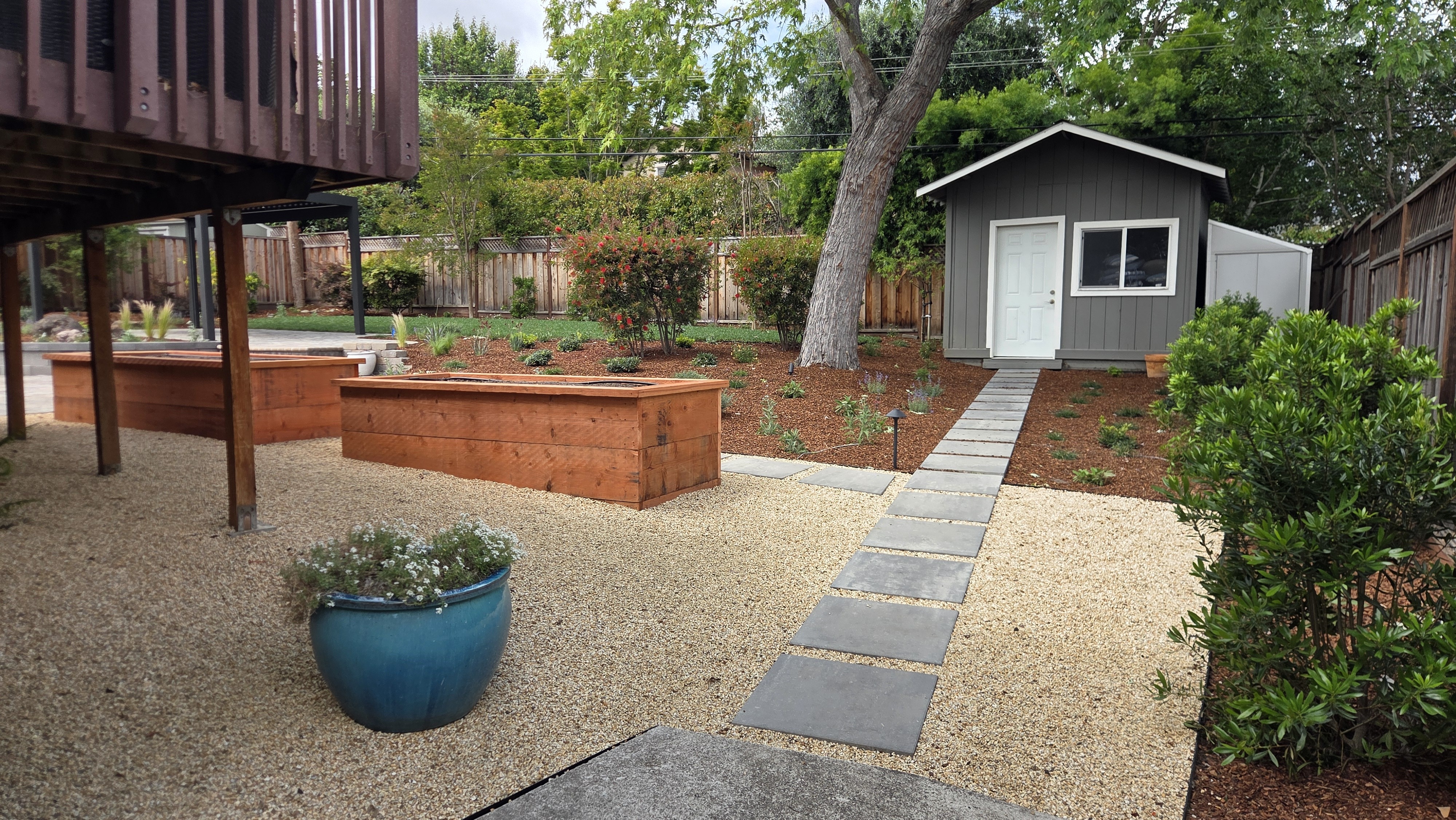 Wide finished low-maintenance landscape with square pavers set in a gravel field leading to a gray shed, cedar raised...
