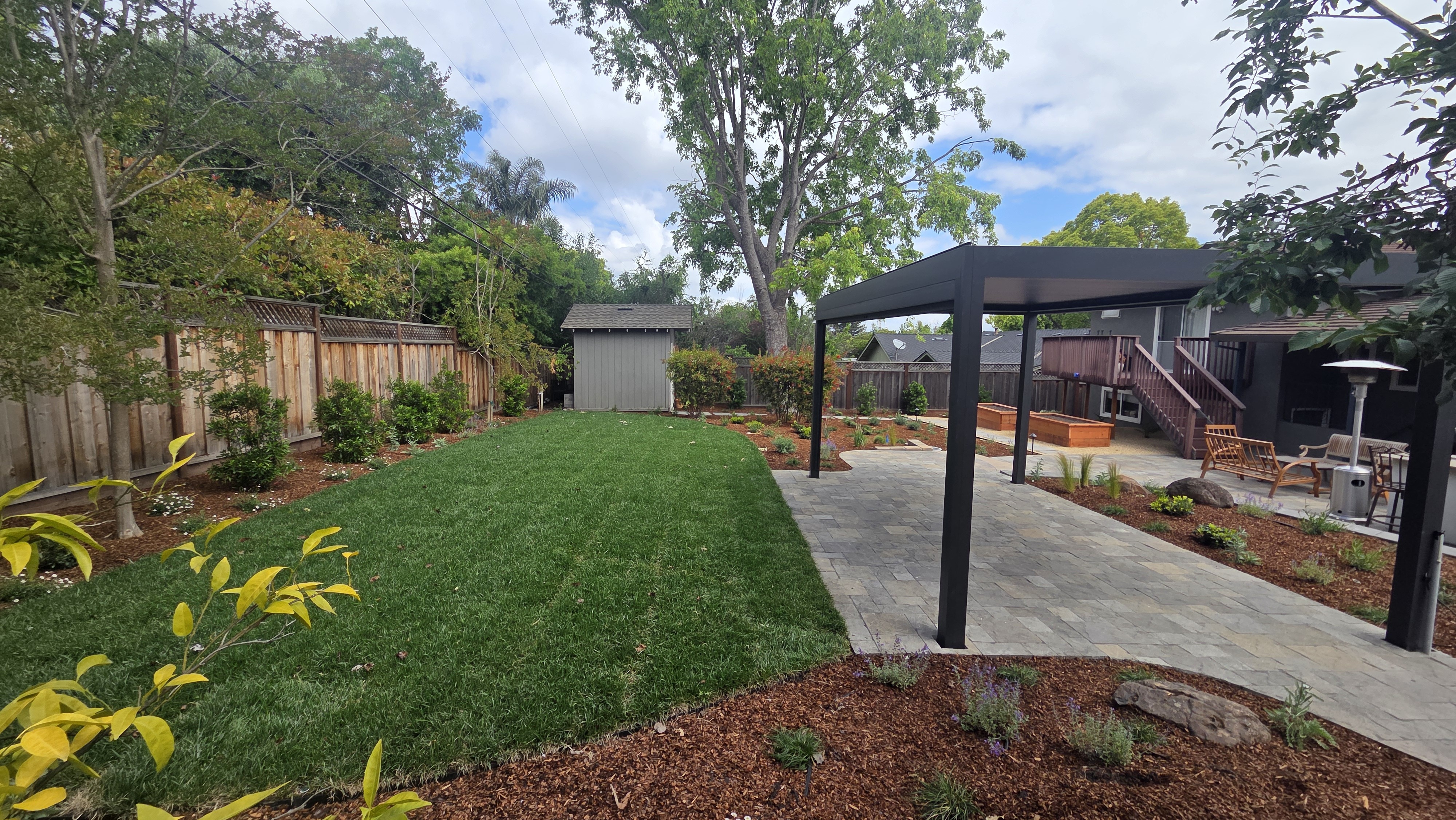 Finished backyard showing a clean green lawn beside the garden shed and the freestanding pergola over the paver patio,...
