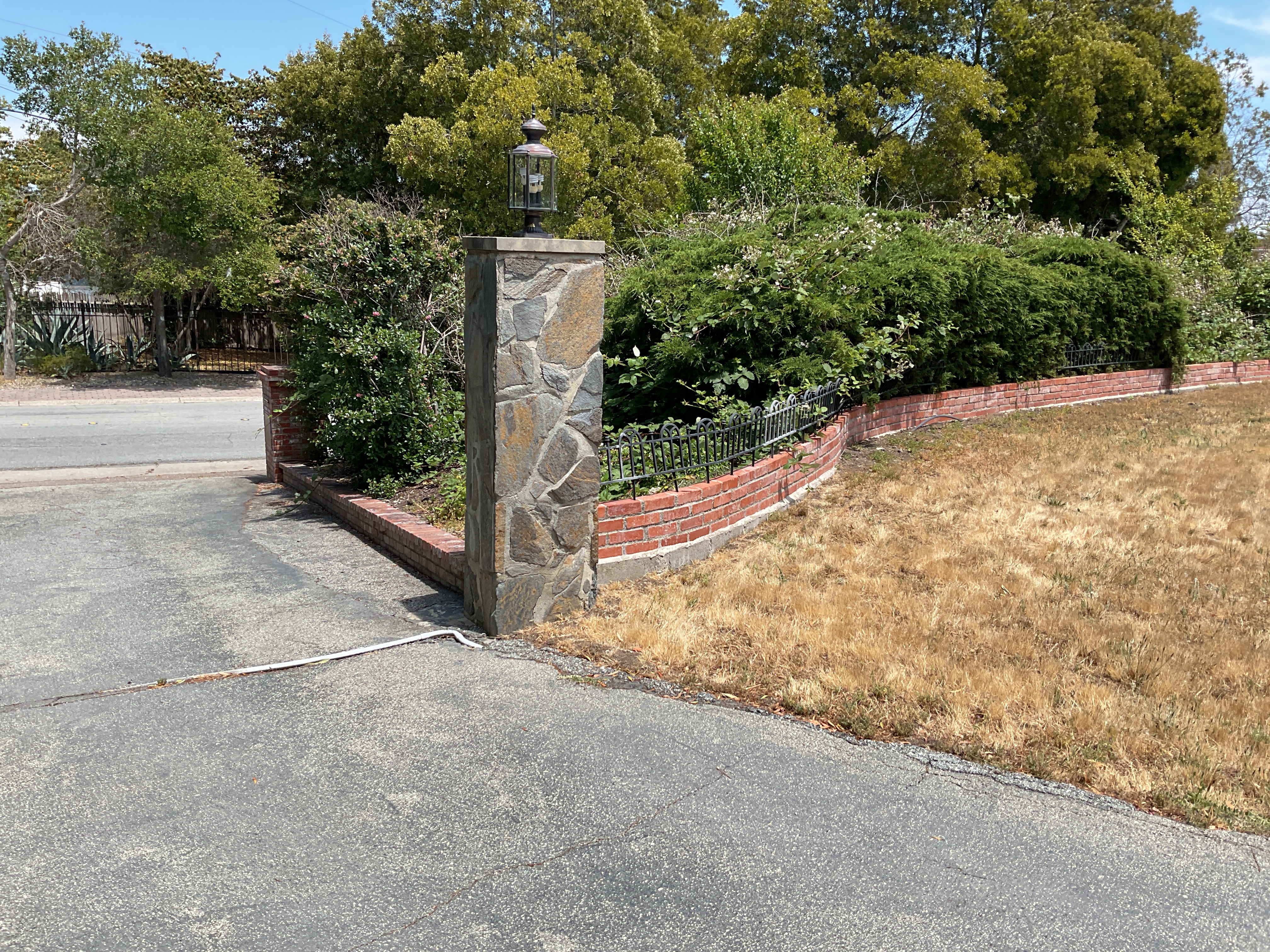 Existing stone entry pillar and brick-and-iron wall beside a dried-out lawn before the rebuild.
