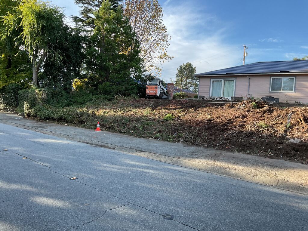 Skid-steer regrading the cleared front slope after the old planting and brick wall were removed.