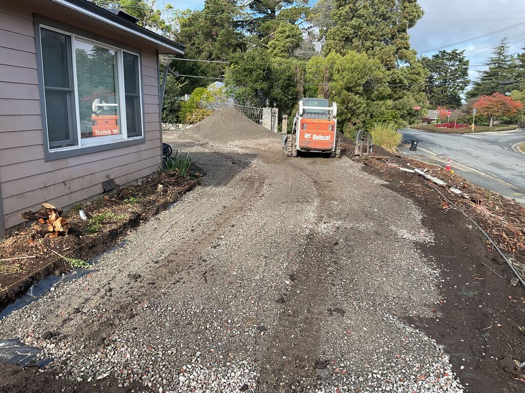 Compacted crushed-rock base spread along the side yard with a skid-steer, ready for paving.
