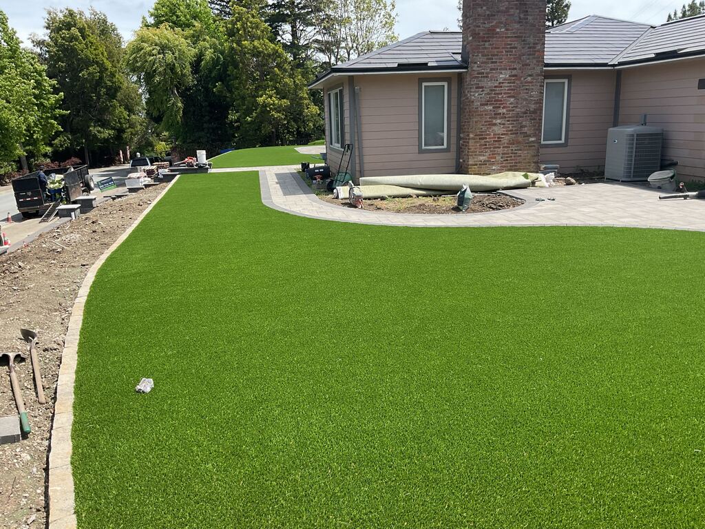 Freshly laid artificial-turf lawn beside the new paver walkway as the installation wraps up.
